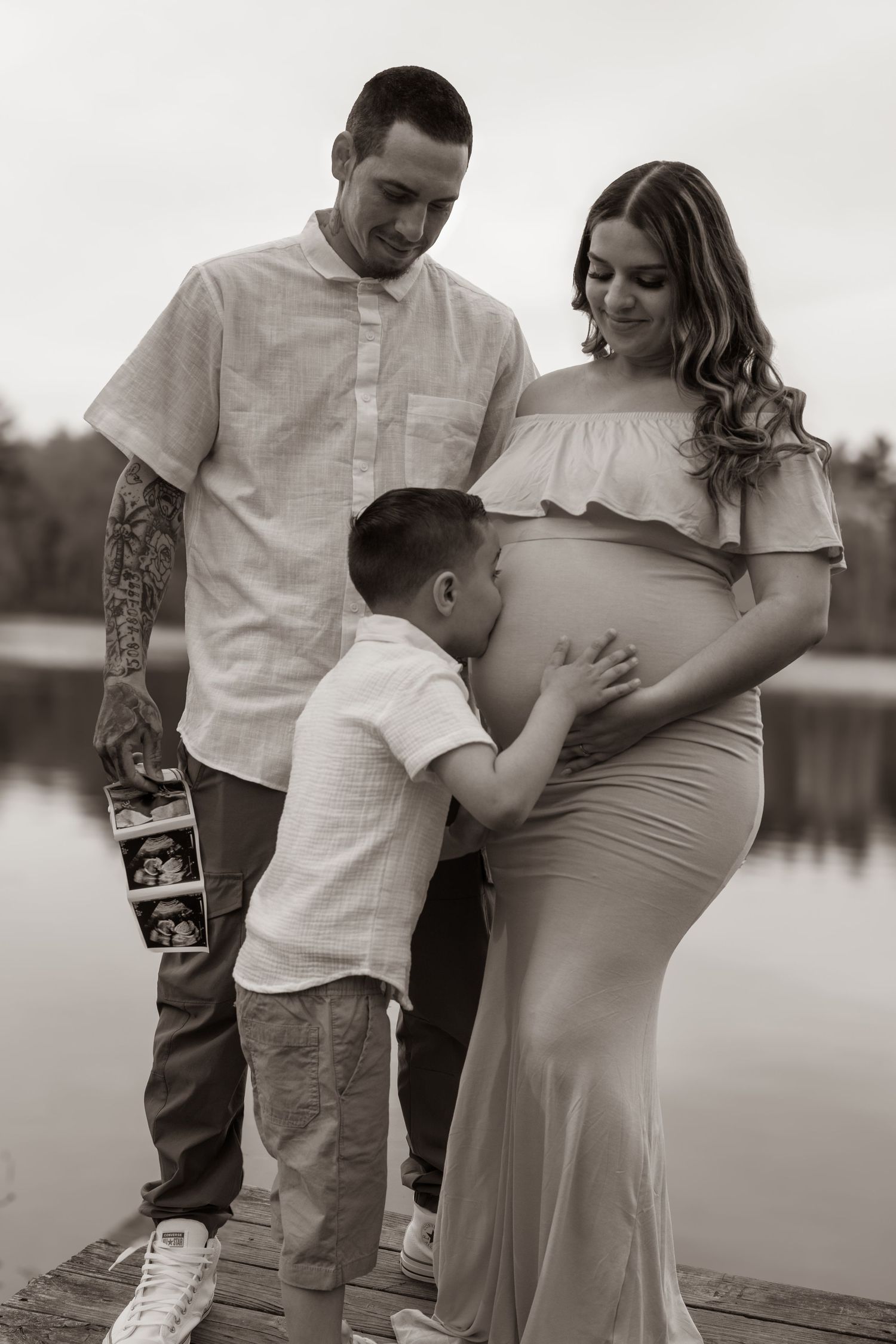 Touching black and white family portrait during maternity photoshoot on dock.