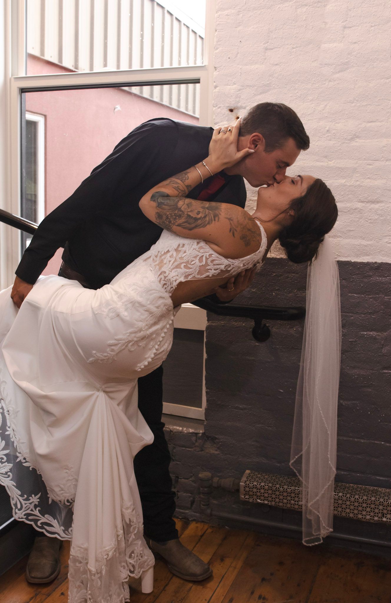 A couple performs dramatic dance dips in formal attire against a white and black painted wall.