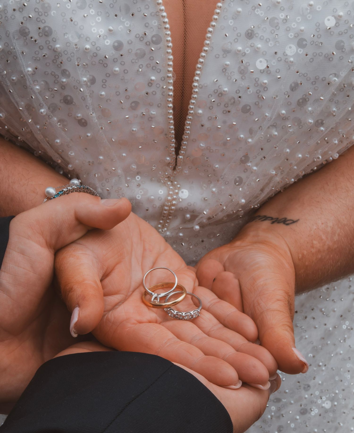 A series of hands holding a sparkling engagement ring against a white beaded or sequined fabric background.