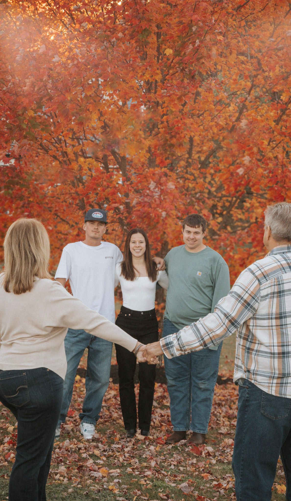 A group stands together against a backdrop of vibrant orange autumn foliage while taking casual photos.