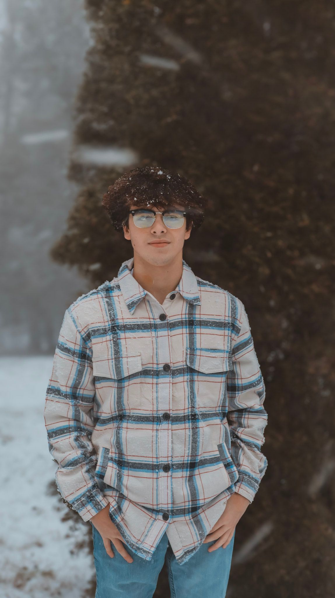 A child wearing a plaid flannel shirt poses outdoors in winter against a snowy background.