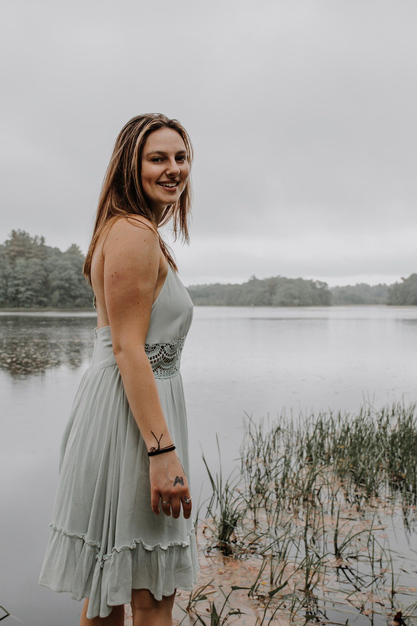 Person in a mint green dress poses by a misty lake surrounded by tall grass and reeds on an overcast day.