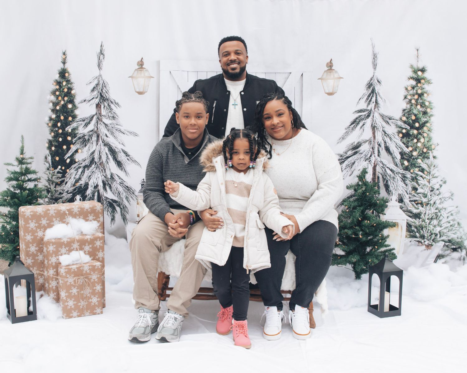 Family posing together in coordinated winter outfits against snowy scene with white barn and evergreens.