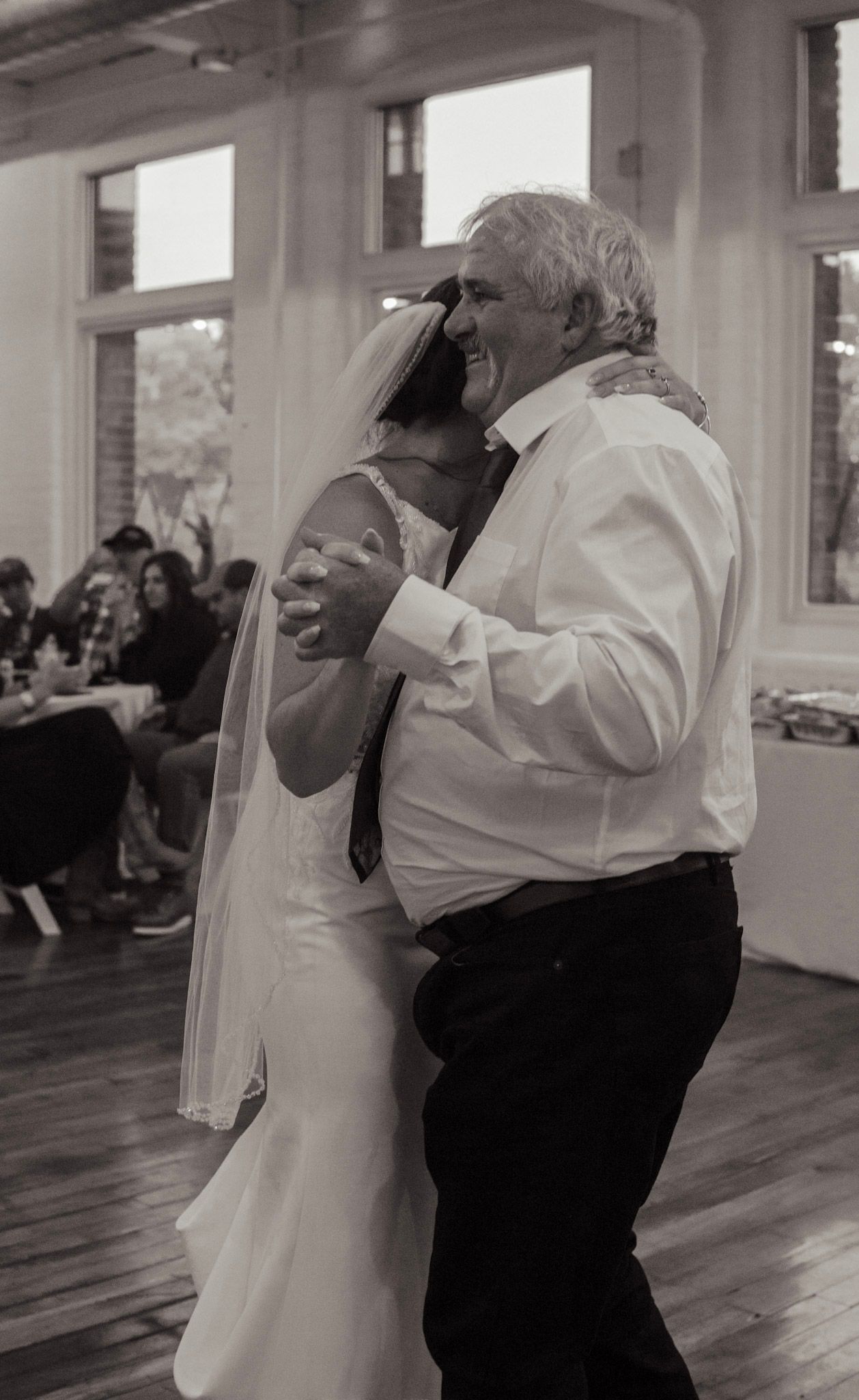 A tender dance moment between a bride in white and an older gentleman at a wedding reception.