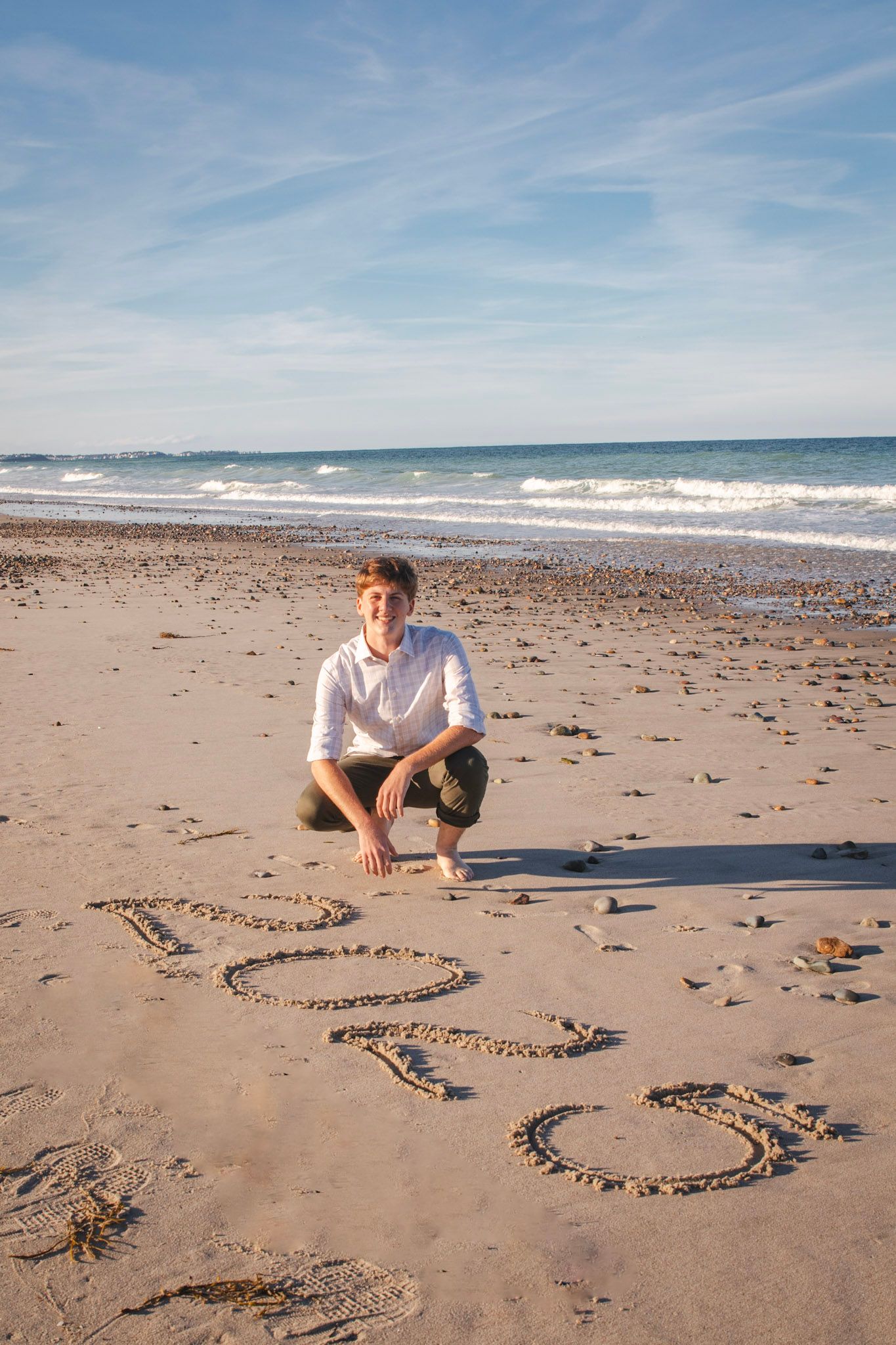 A series of heart shapes drawn in the sand on a sunny beach with ocean waves in the background.