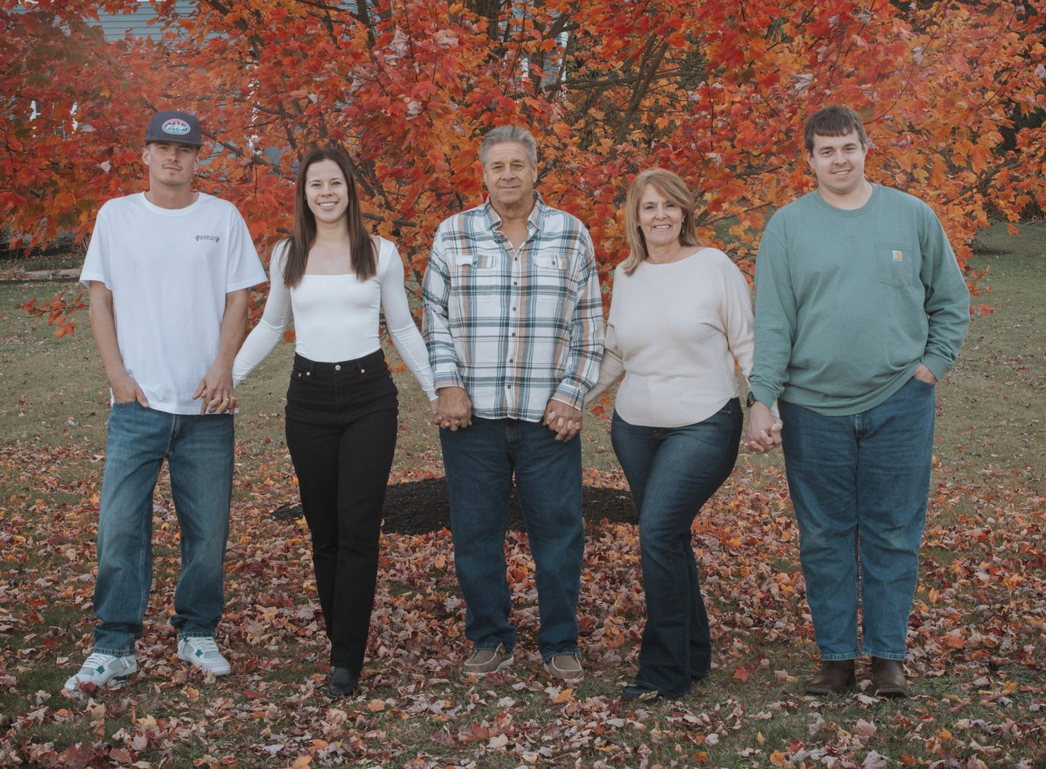 Five people stand together in a row against a backdrop of bright orange fall foliage and scattered leaves.