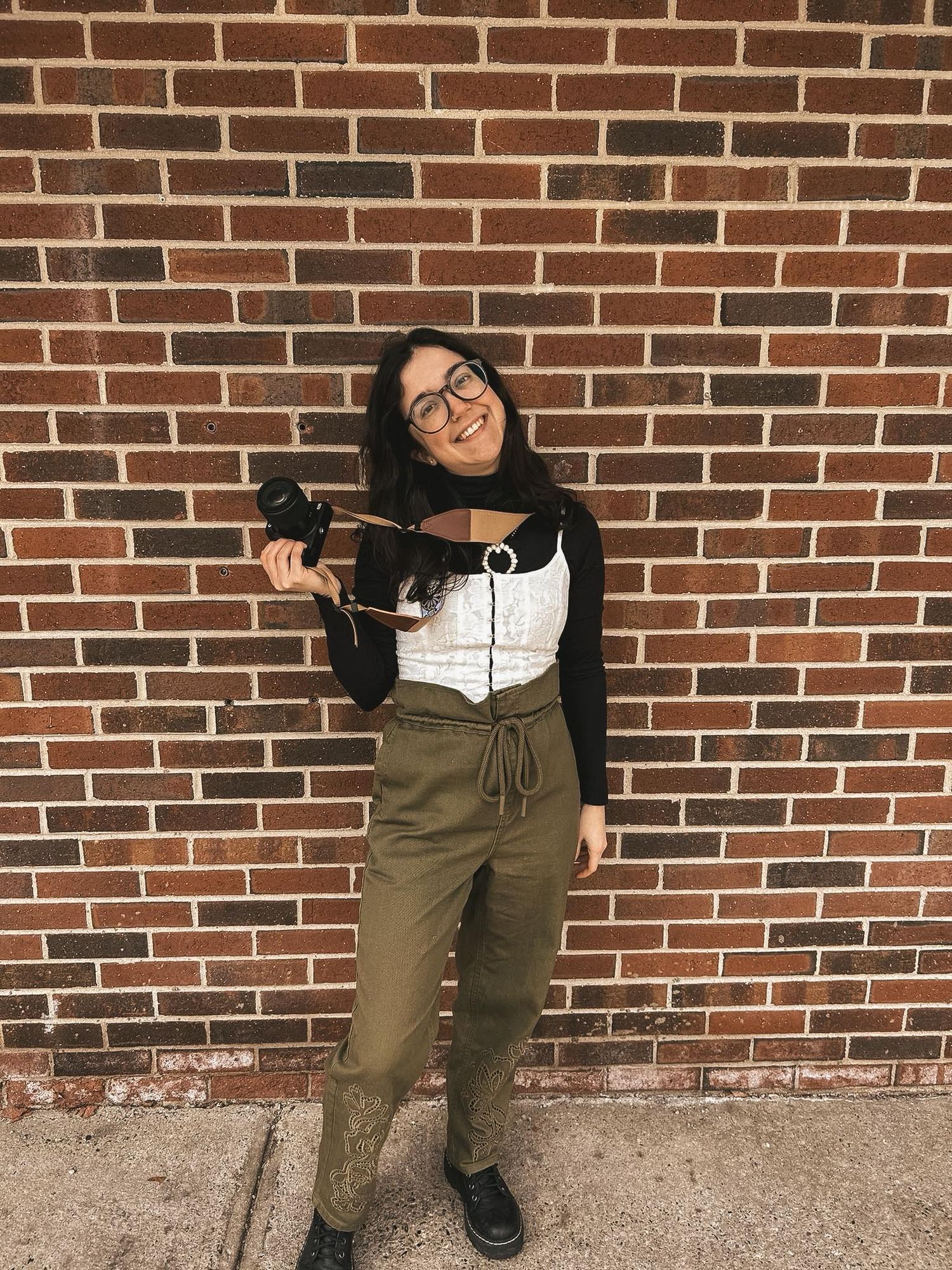 Person wearing glasses and black sweater poses against brick wall in olive green jogger pants showing different sitting positions.