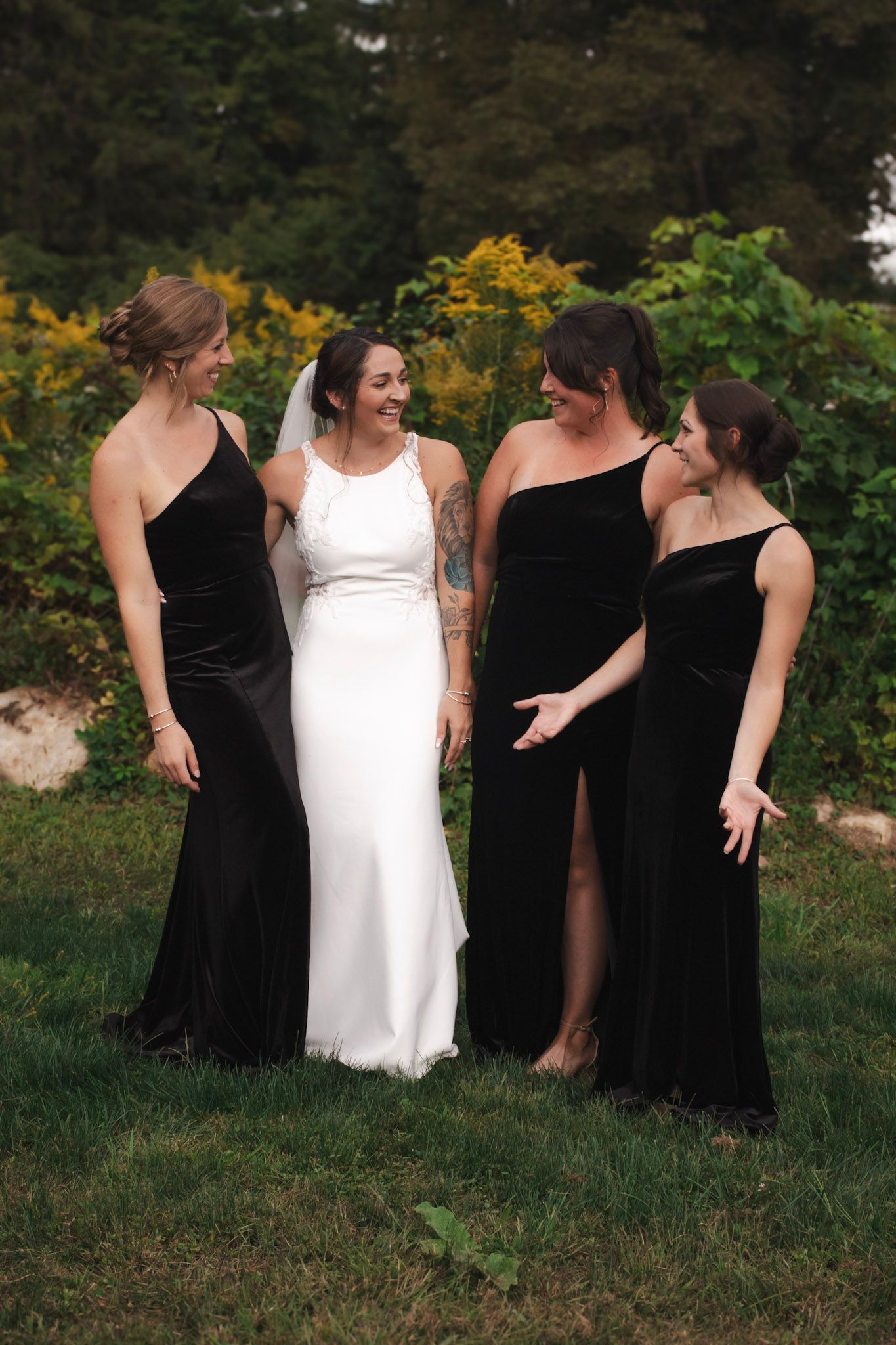 Wedding party in black bridesmaid dresses and white bridal gown posing together in a garden setting.