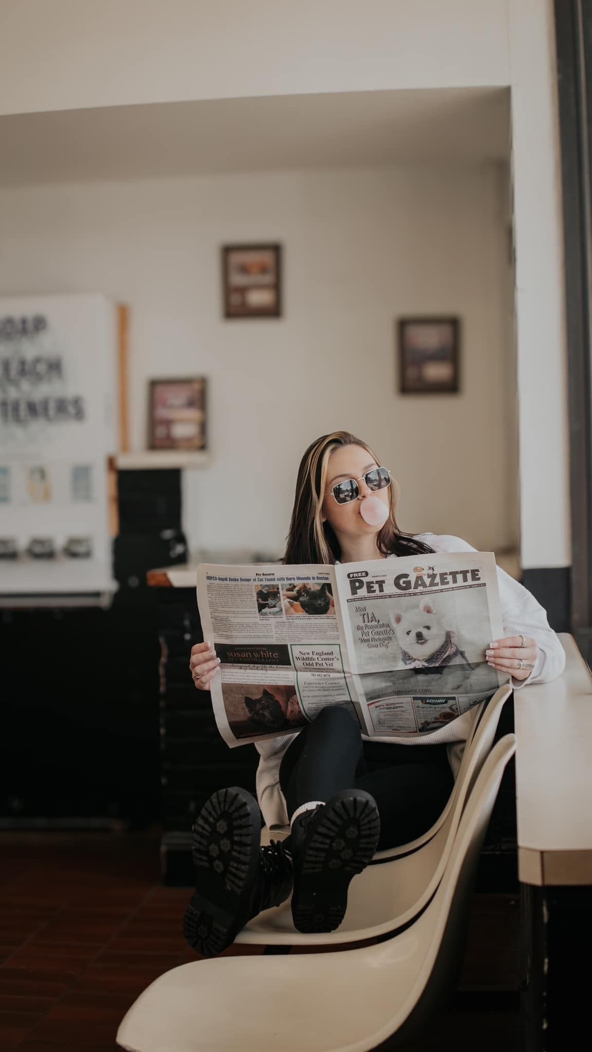 Person in chunky boots sits casually in modern chair while reading Pet Gazette newspaper.