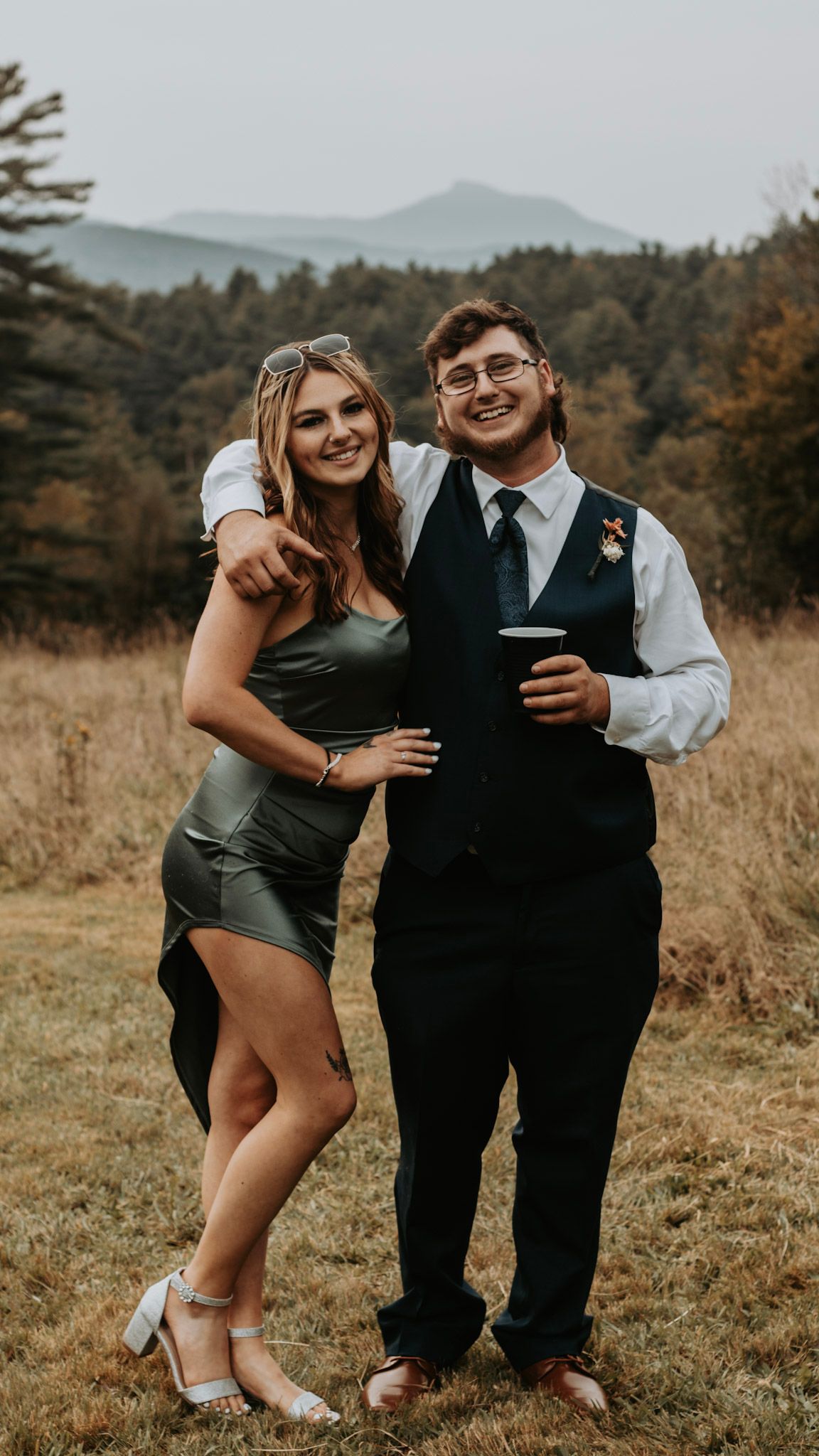 A couple shares a candid moment at an outdoor celebration with mountain views and fall foliage.