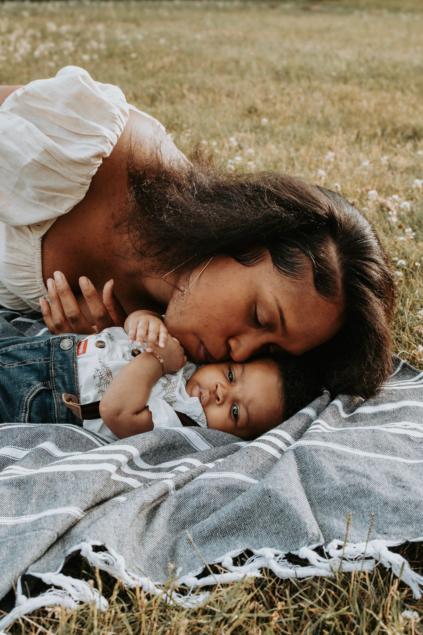 Parent and child lying on a gray blanket in a grassy field sharing an intimate moment.