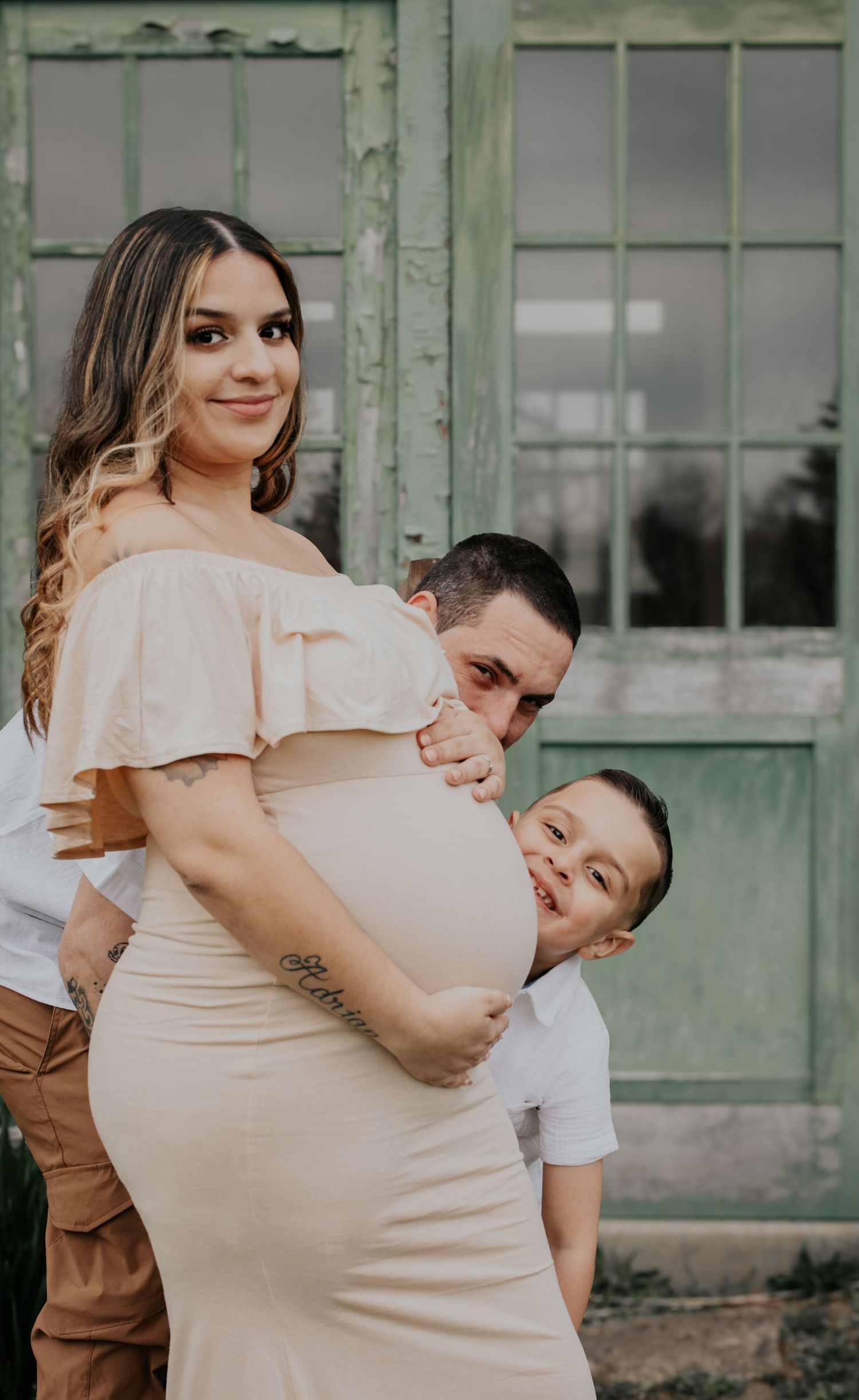 Intimate maternity photography session against weathered green architecture.