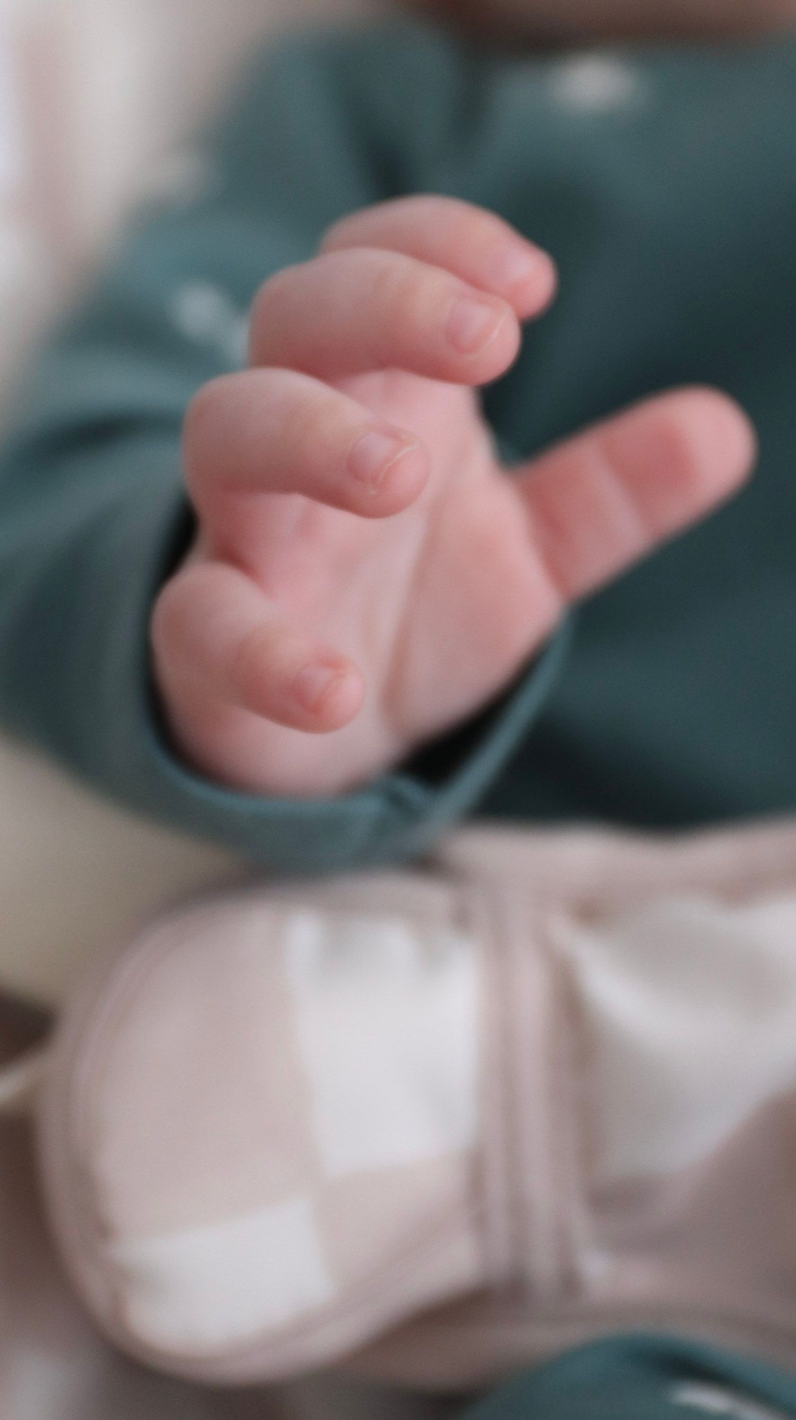 Delicate newborn baby fingers and hands photographed in soft focus against a teal background.