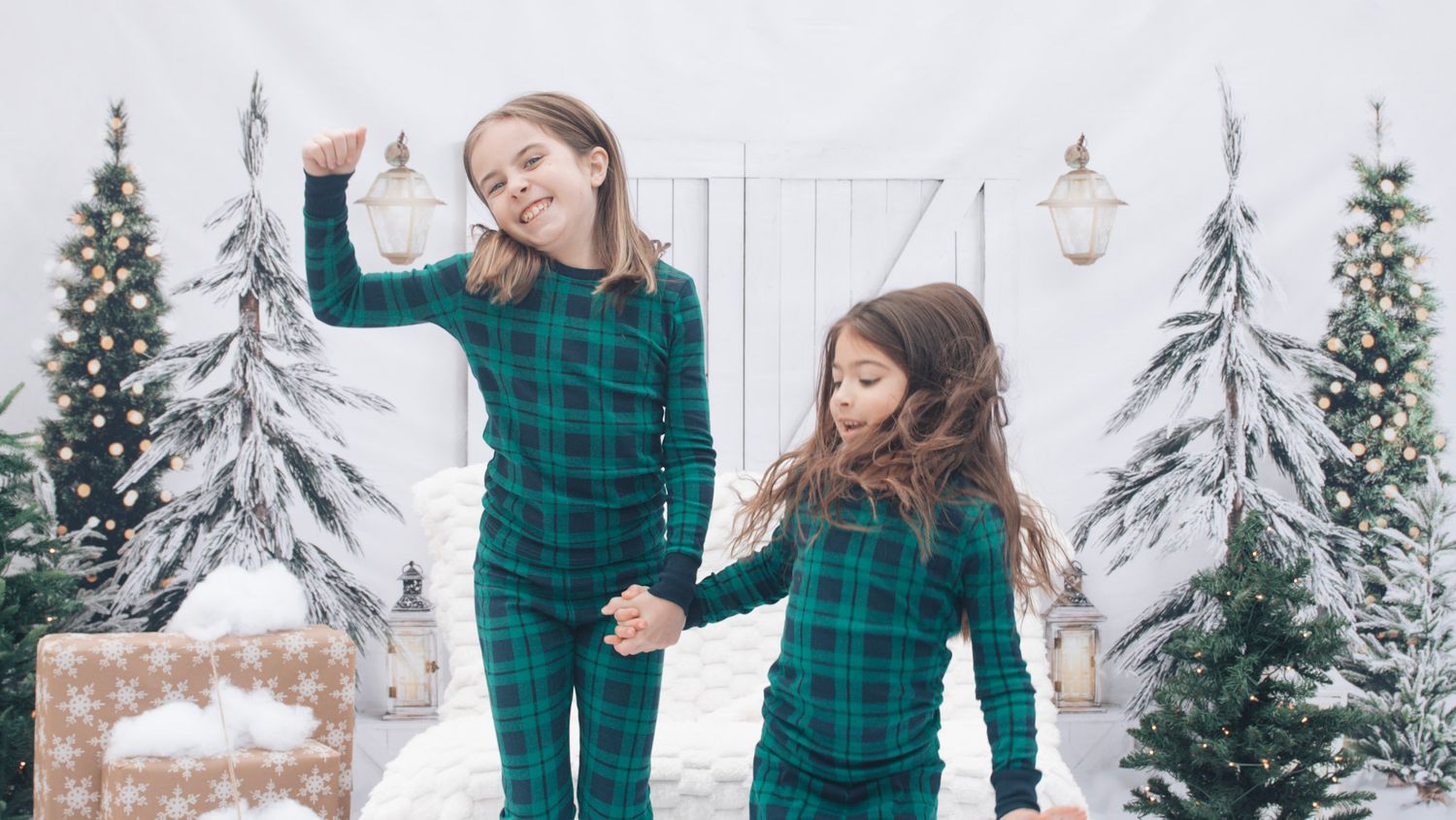 Family in coordinated green plaid outfits playing in snow against white barn backdrop.