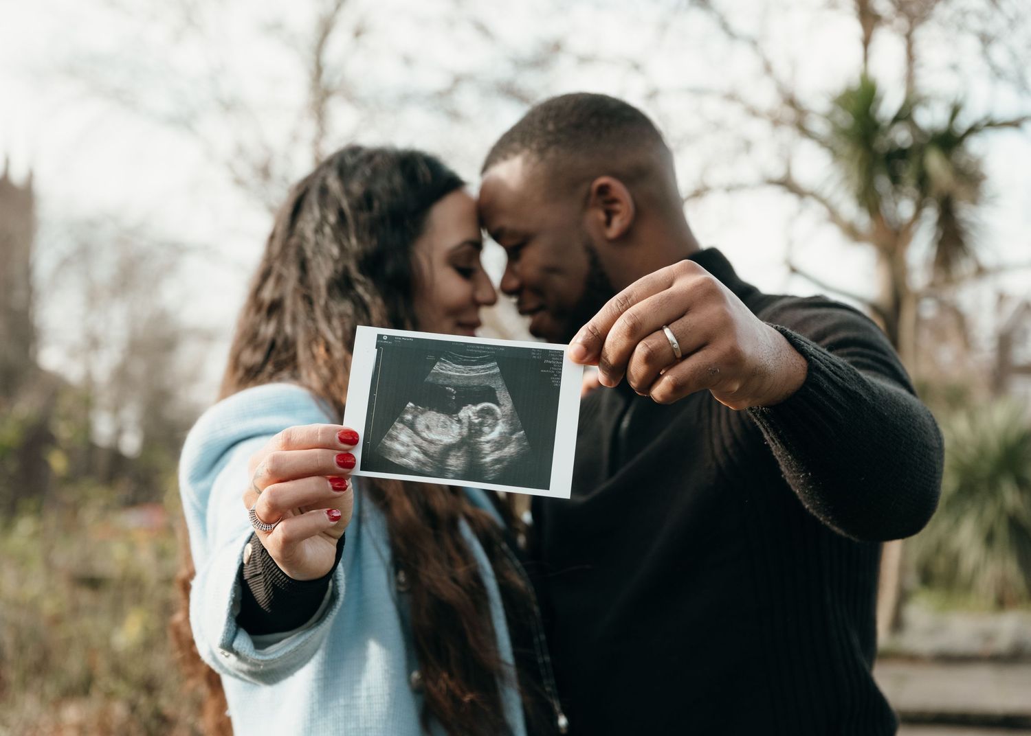 Couple sharing ultrasound photos in an outdoor setting during autumn.