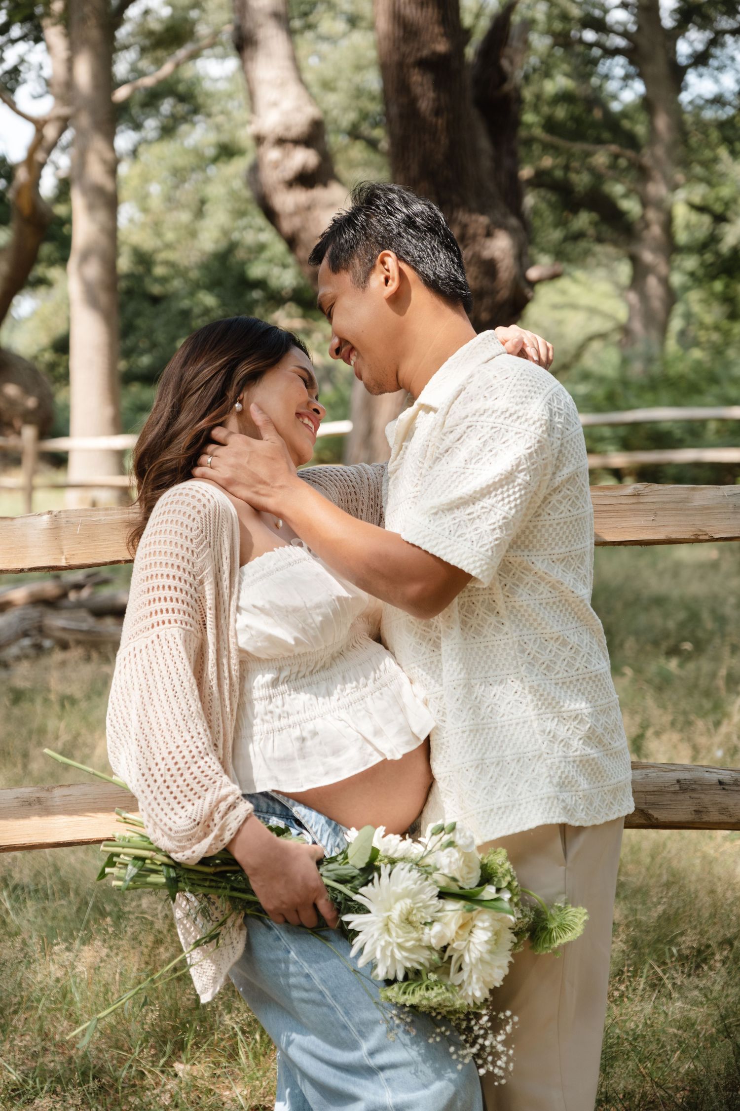 Romantic couple's maternity photos in white outfits near wooden fence.
