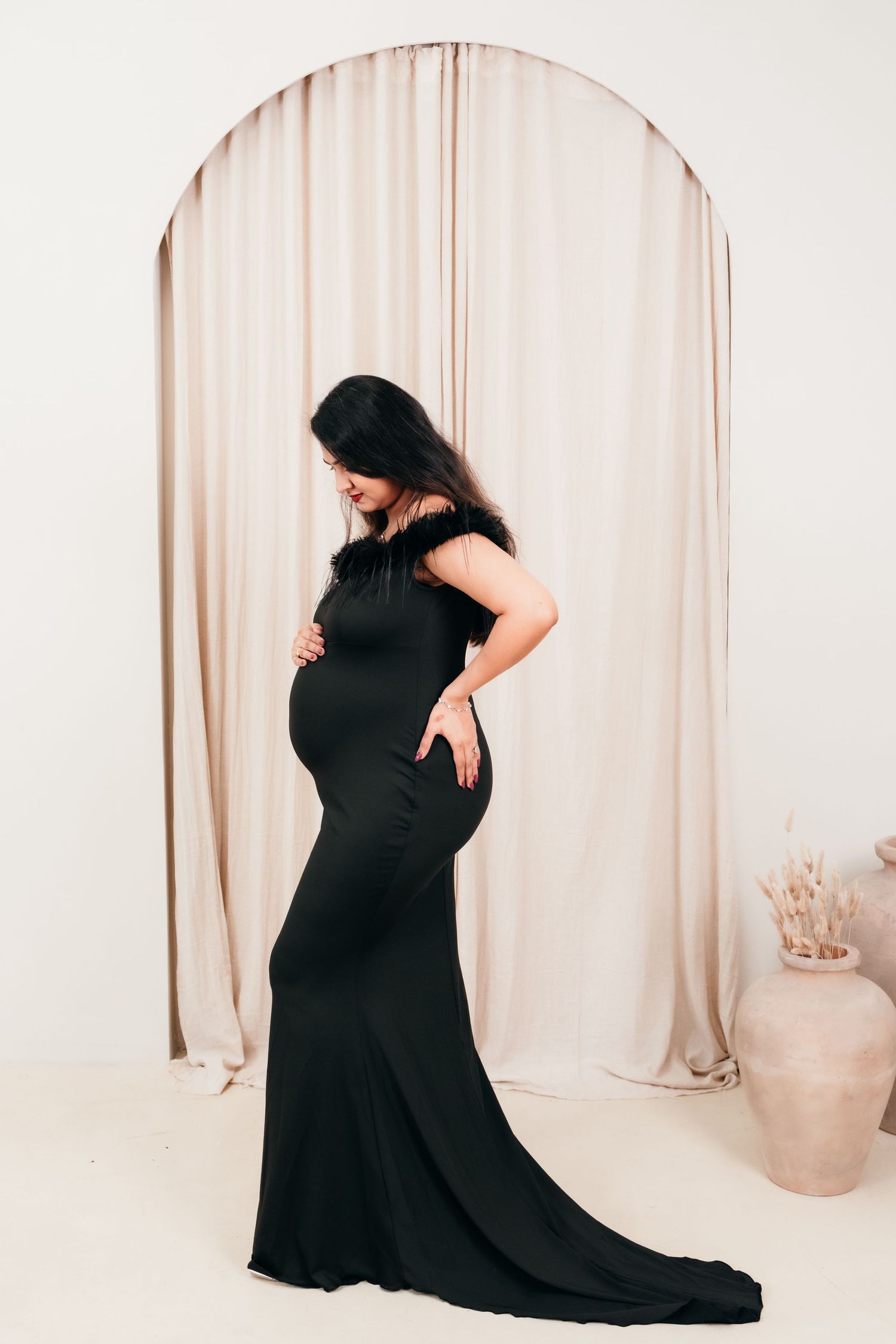 Elegant maternity photos in a black flowing dress against a neutral backdrop.