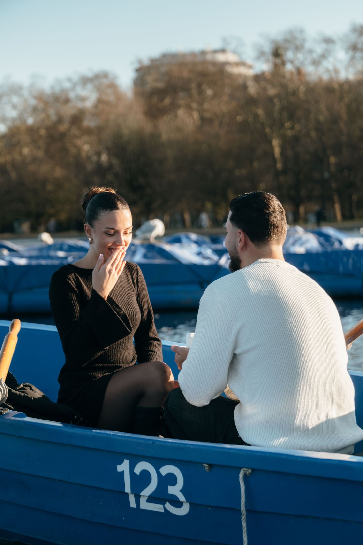 A couple shares an intimate moment in a blue rowboat numbered 123 on a serene lake during sunset.