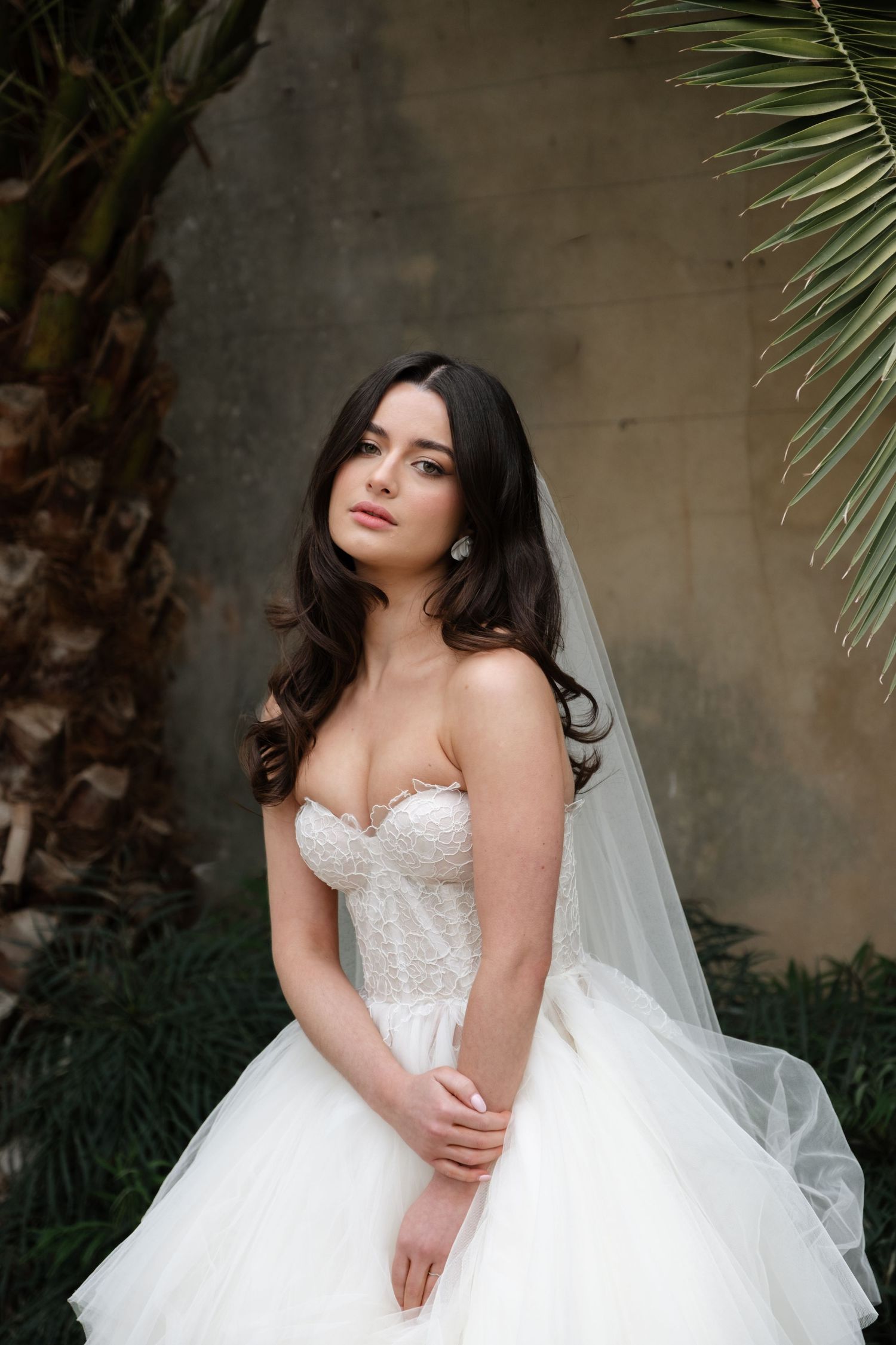Beautiful bridal portrait featuring a strapless white ballgown with sweetheart neckline and flowing veil against tropical foliage.