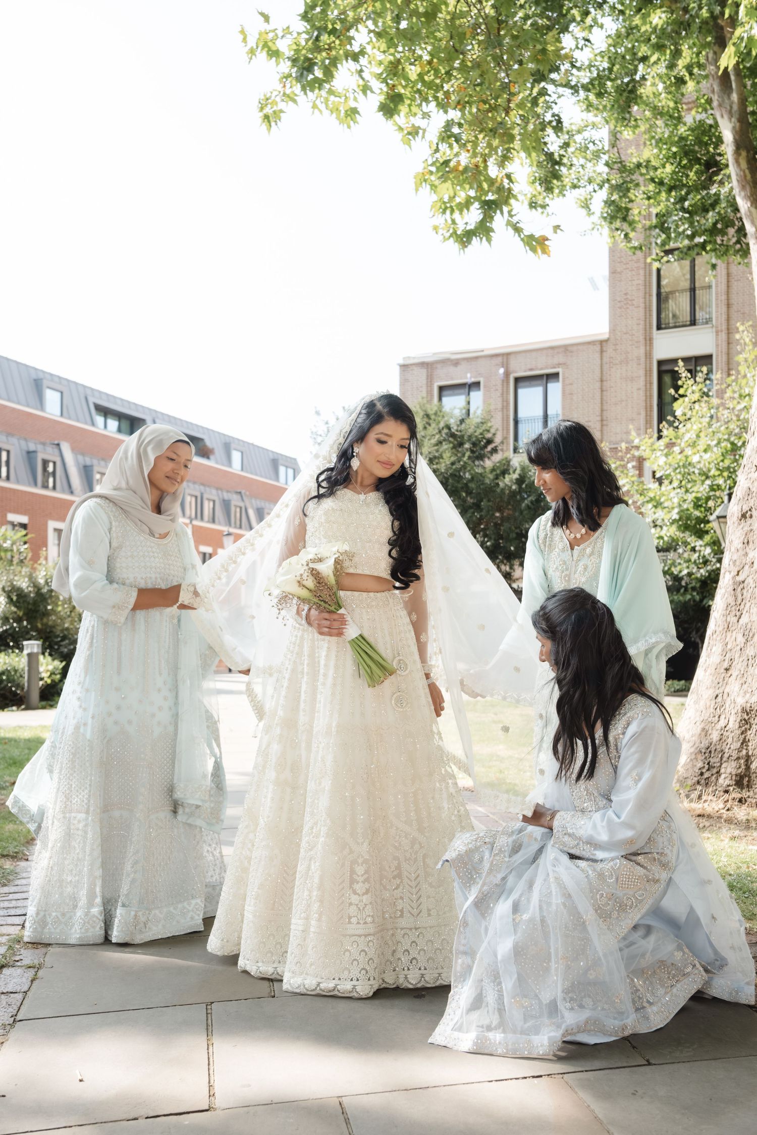 Four women in white traditional South Asian attire pose together outdoors.
