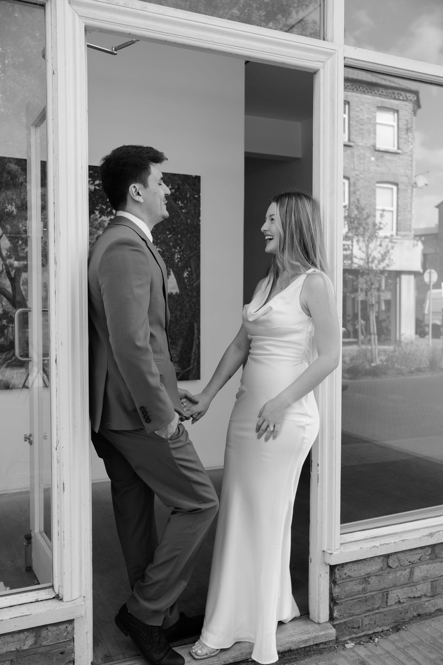Wedding couple poses by large windows in black and white photography sequence.