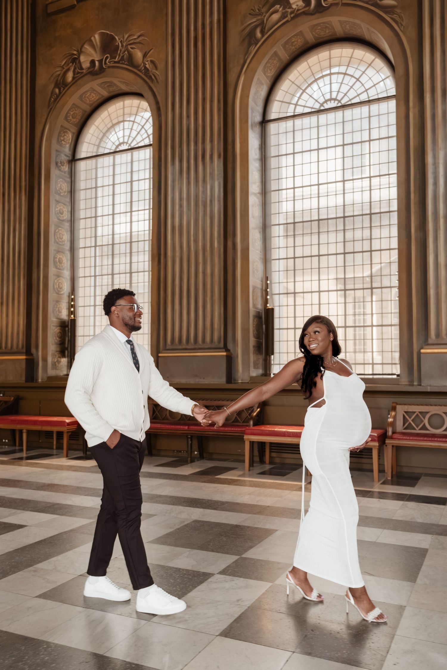 Dancing couple in black and white attire move gracefully across a marble floor in an ornate historic hall.