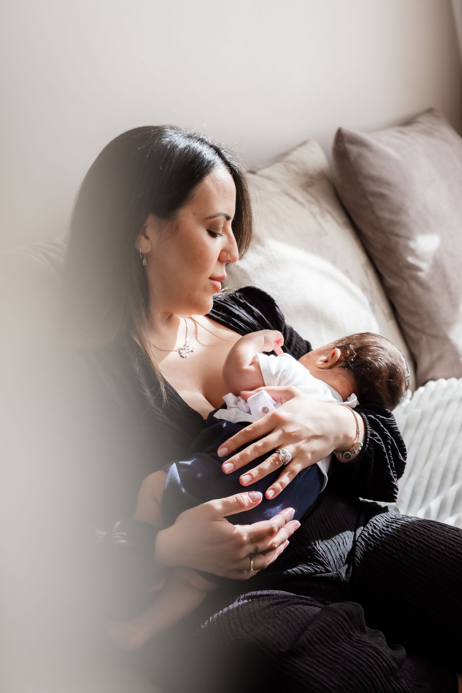 A mother tenderly breastfeeds her newborn baby while sitting on a couch at home.