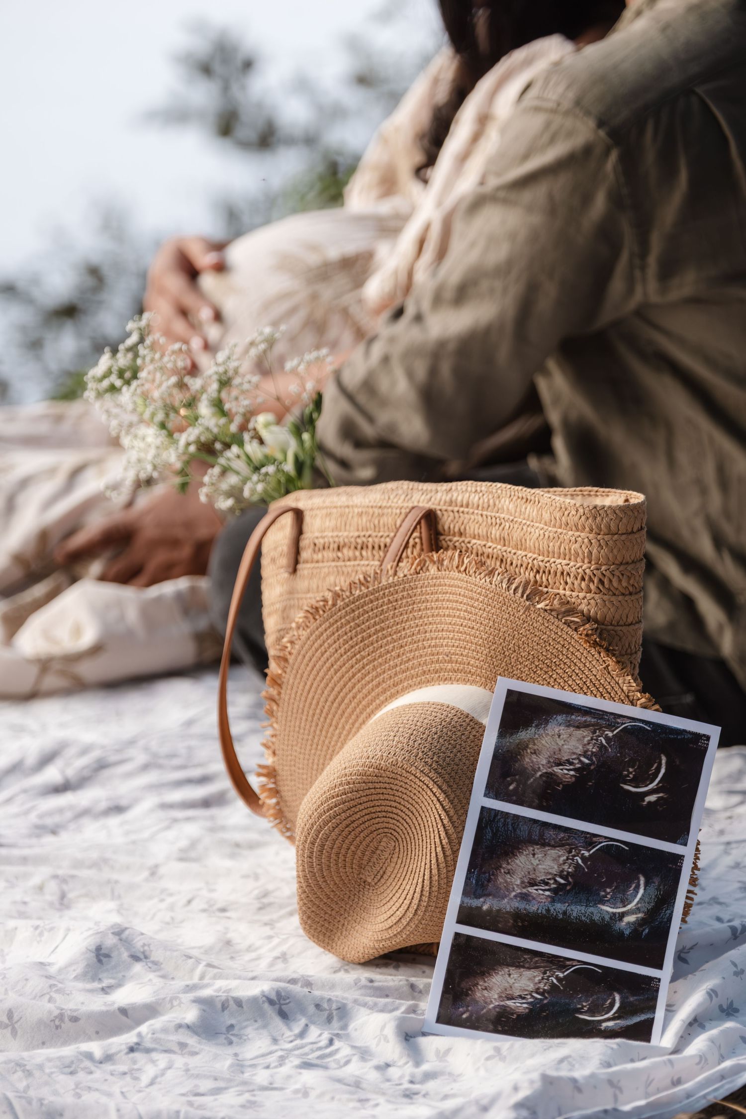 Straw beach bag and ultrasound photos arranged on white textured surface.