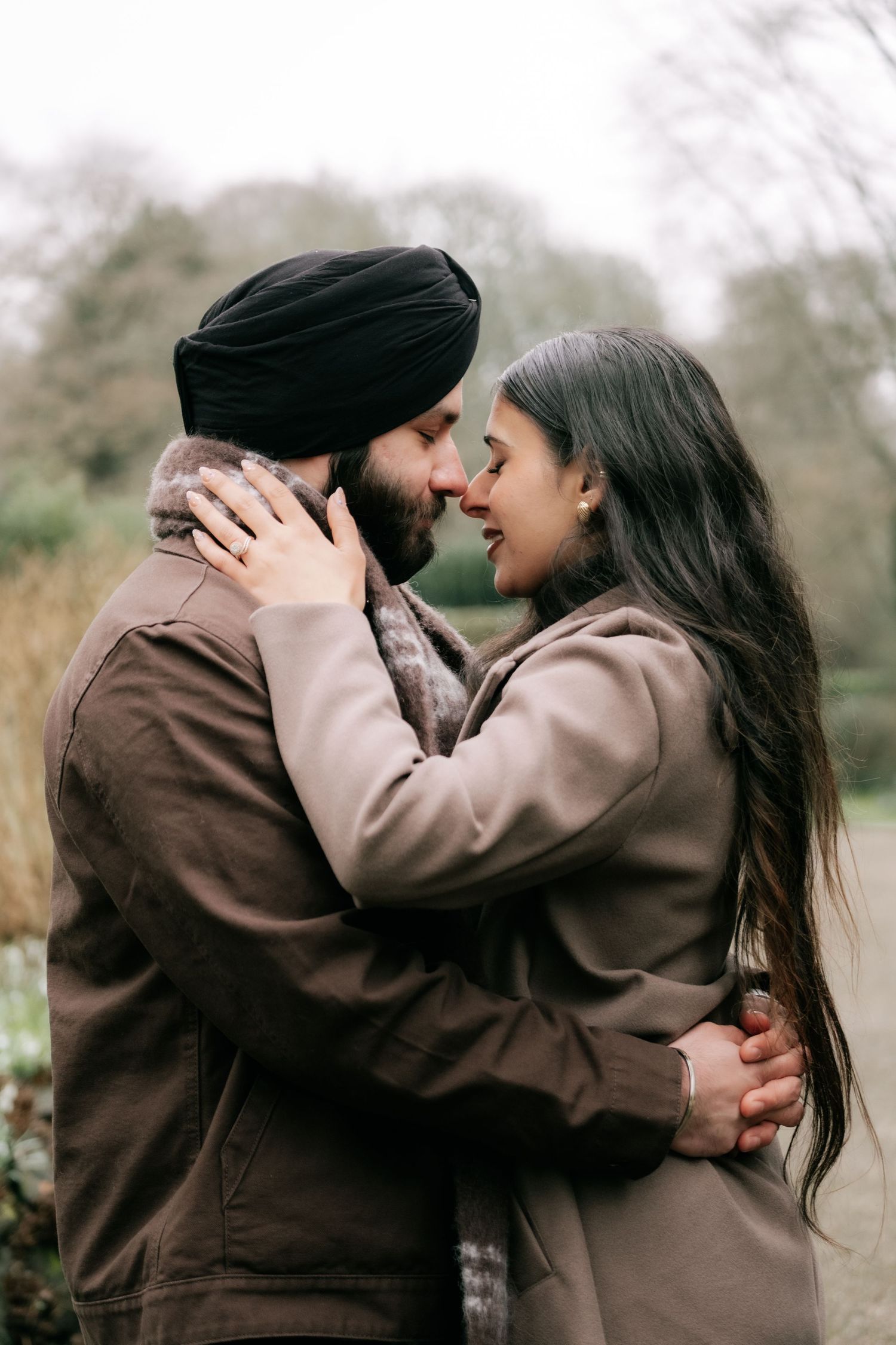 An intimate moment between a couple in matching brown coats against a natural backdrop.