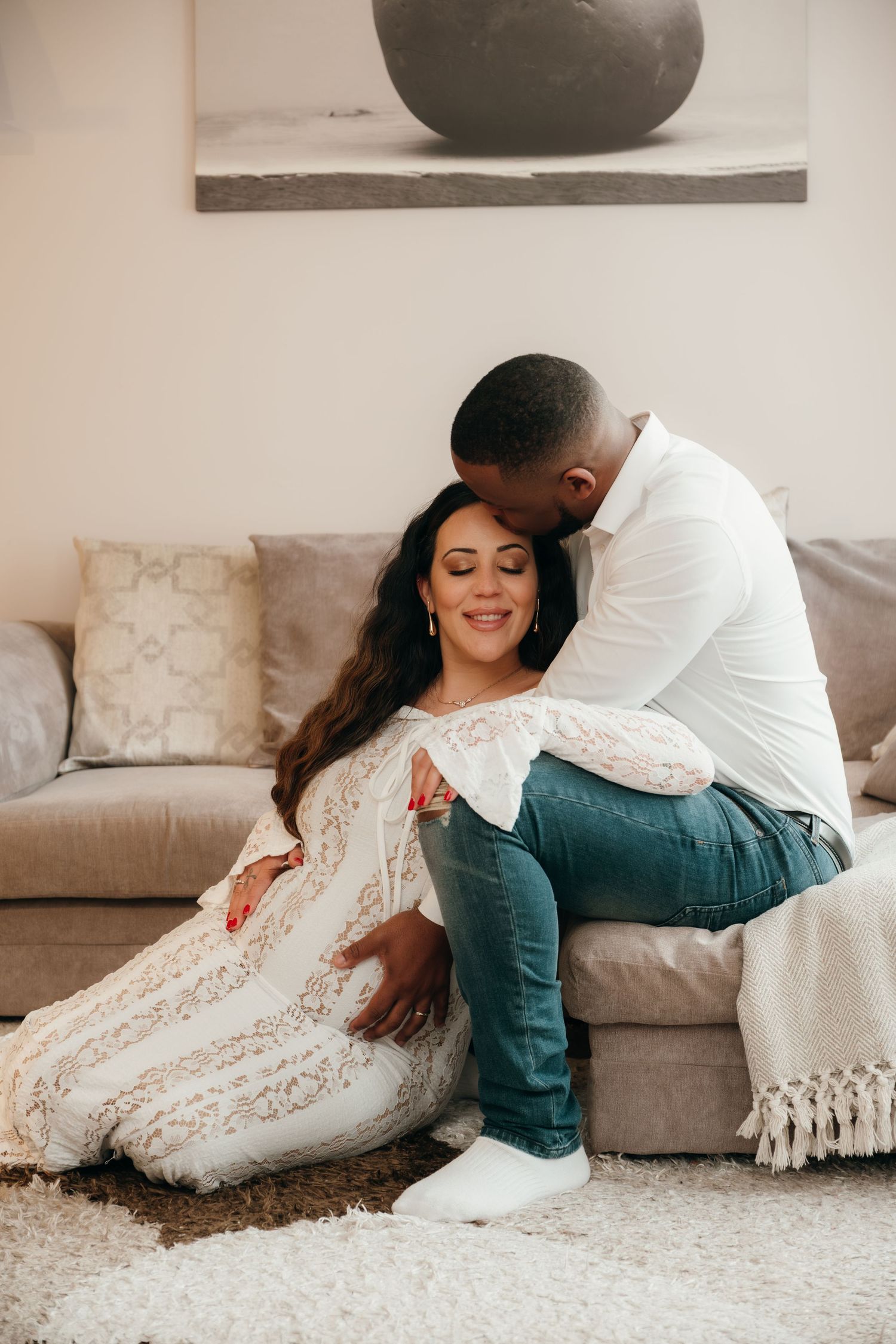 Intimate couple's photo session on a cozy gray couch with white throw pillows.
