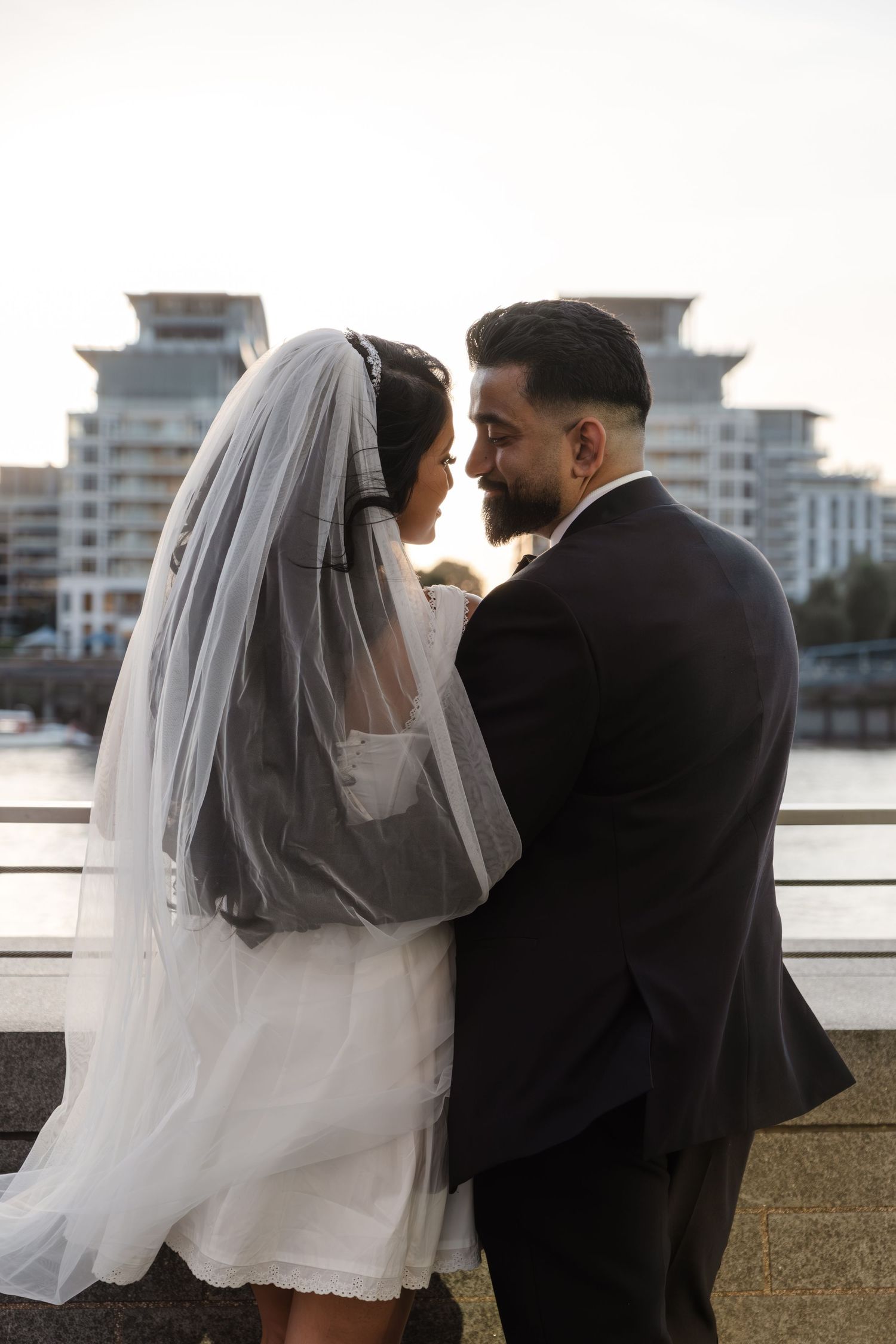 Couple in wedding attire sharing an intimate moment by the waterfront during golden hour.