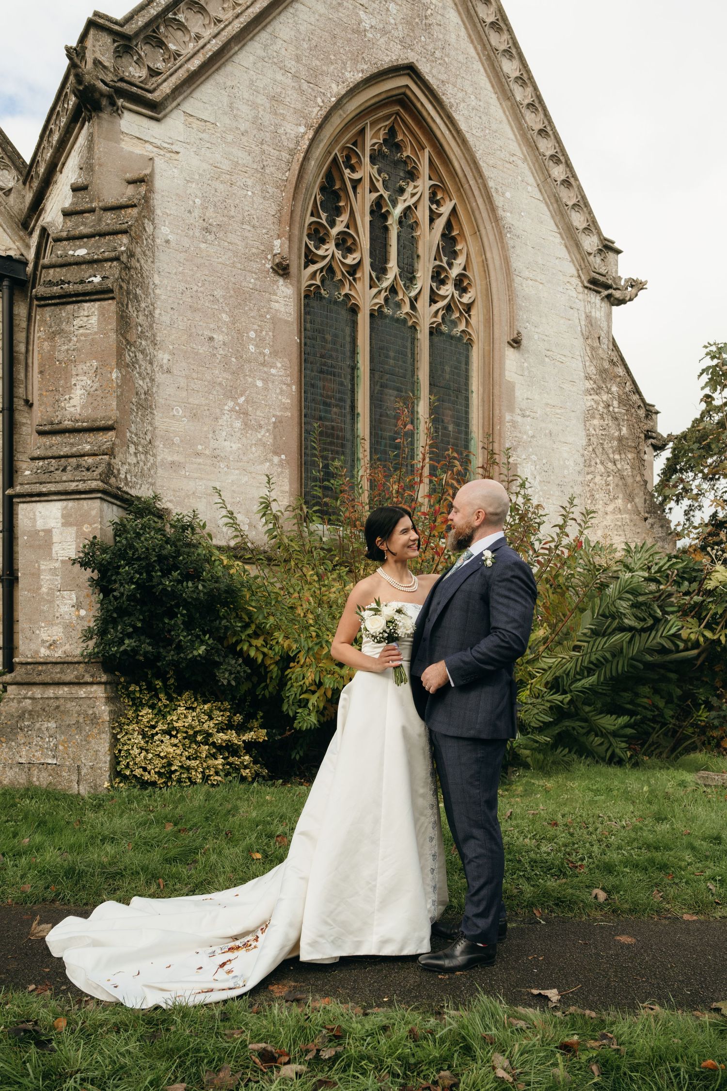 A wedding couple poses outside a historic stone church with gothic architecture and stained glass windows.