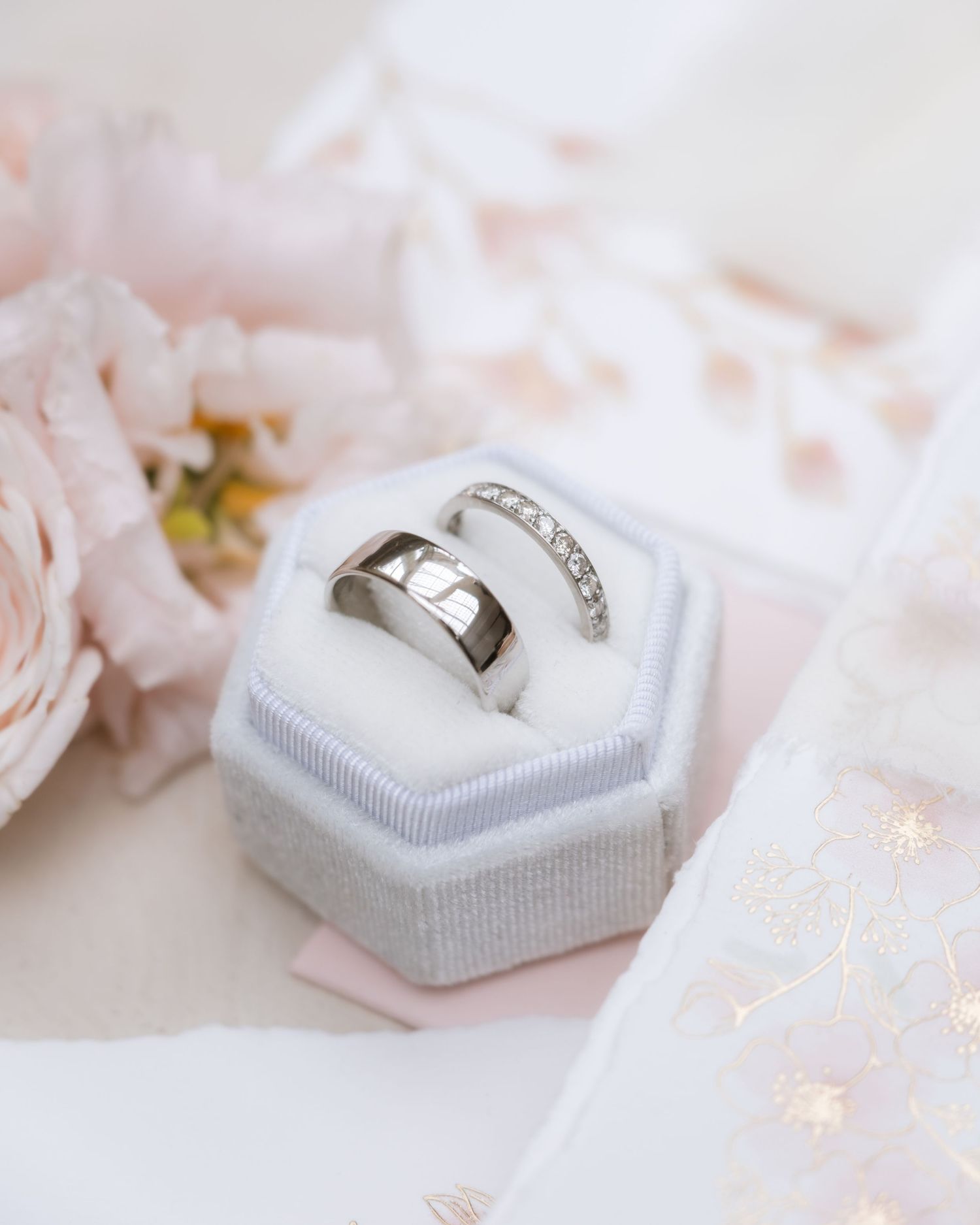 Wedding rings nestled in a light gray velvet ring box with soft pink details.