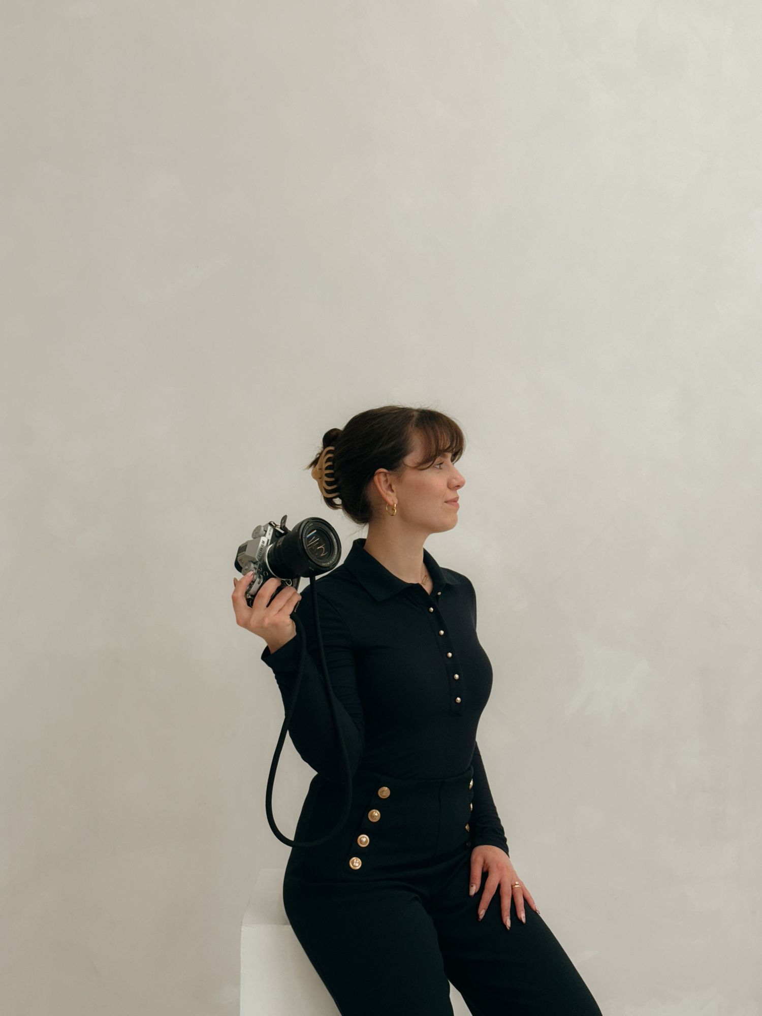 Photographer in black clothing poses with camera against white background.
