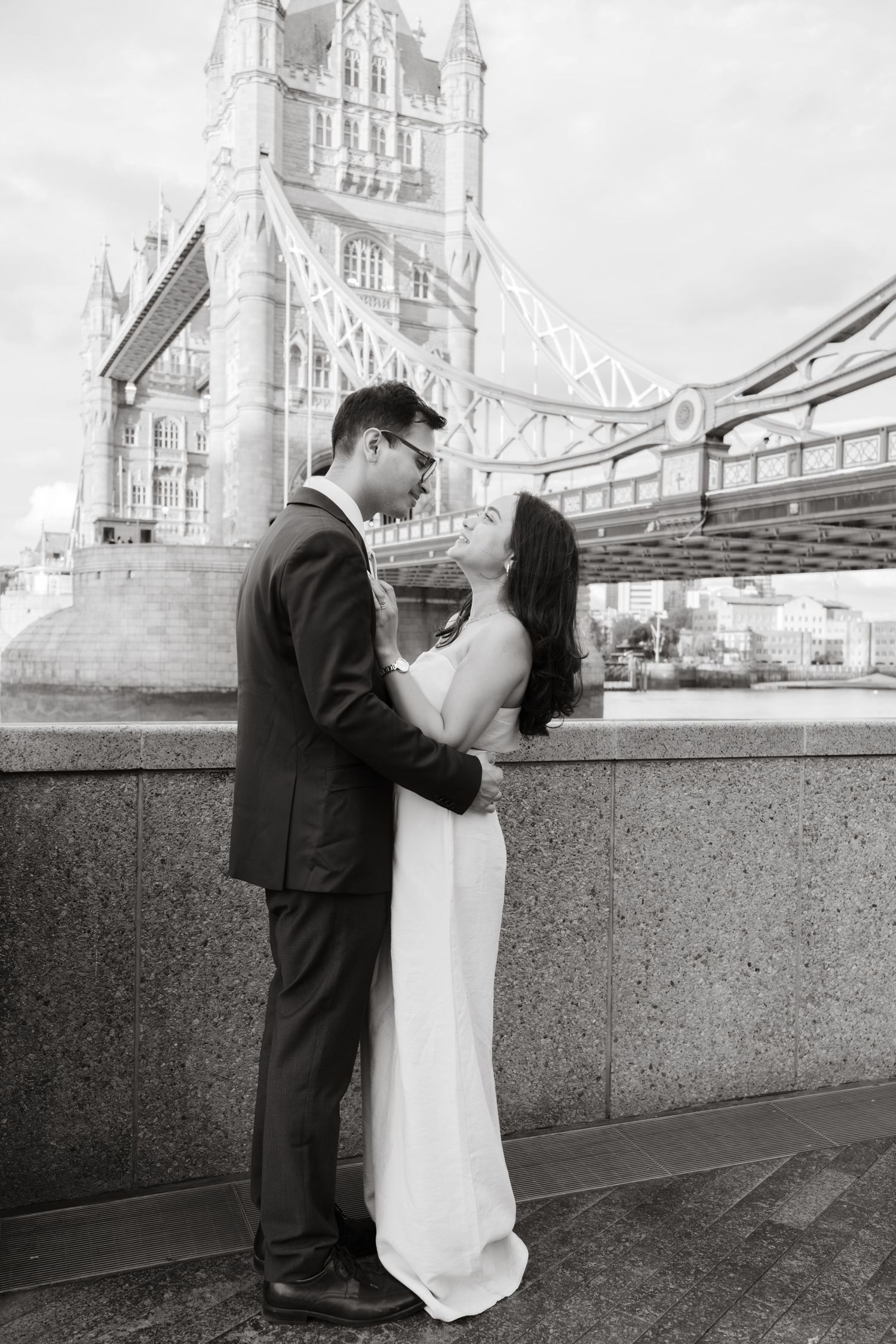 A couple in wedding attire poses near Tower Bridge in London in a series of black and white photos.