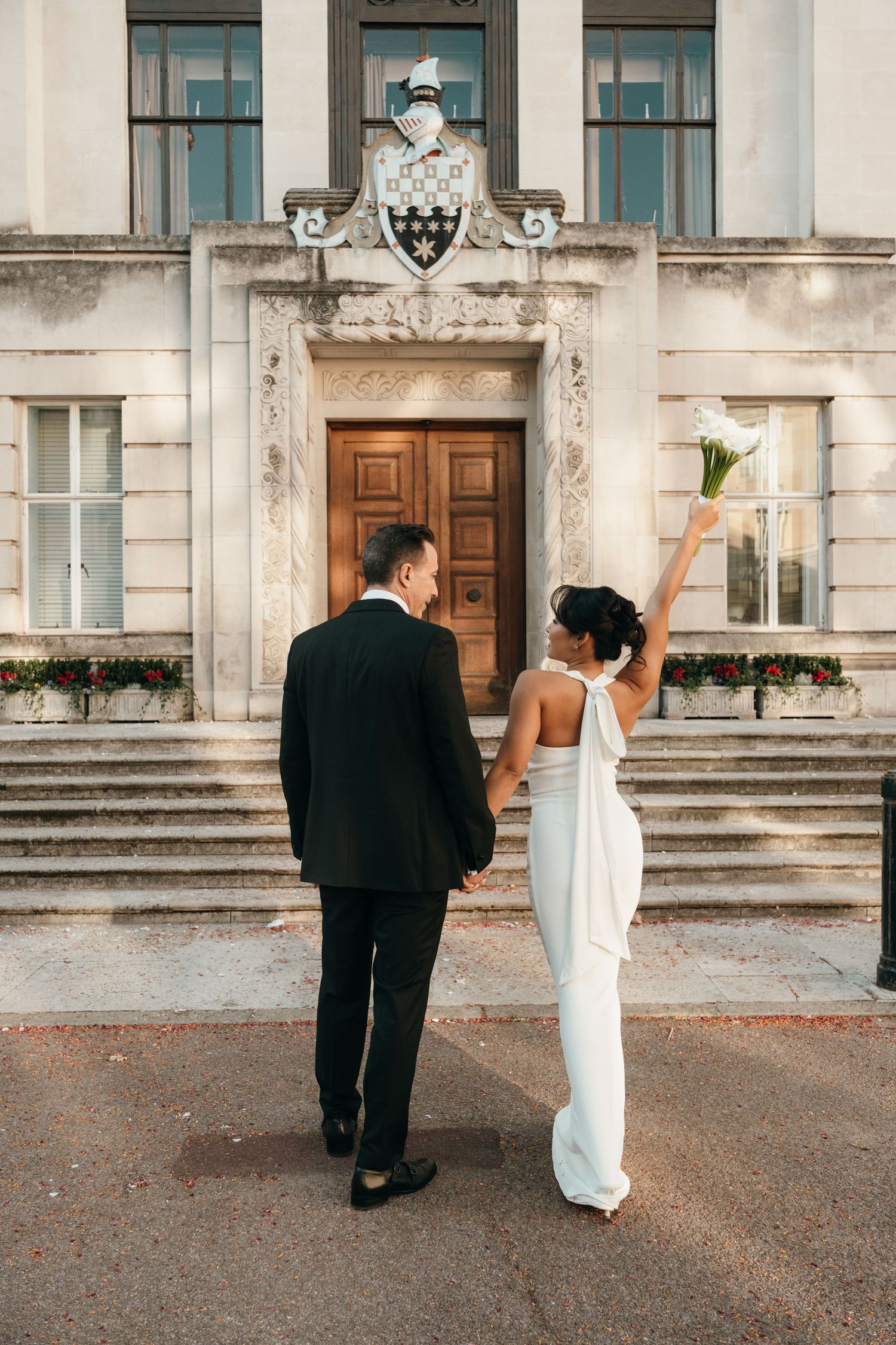 Newlyweds walking hand in hand outside historic building with architectural details.