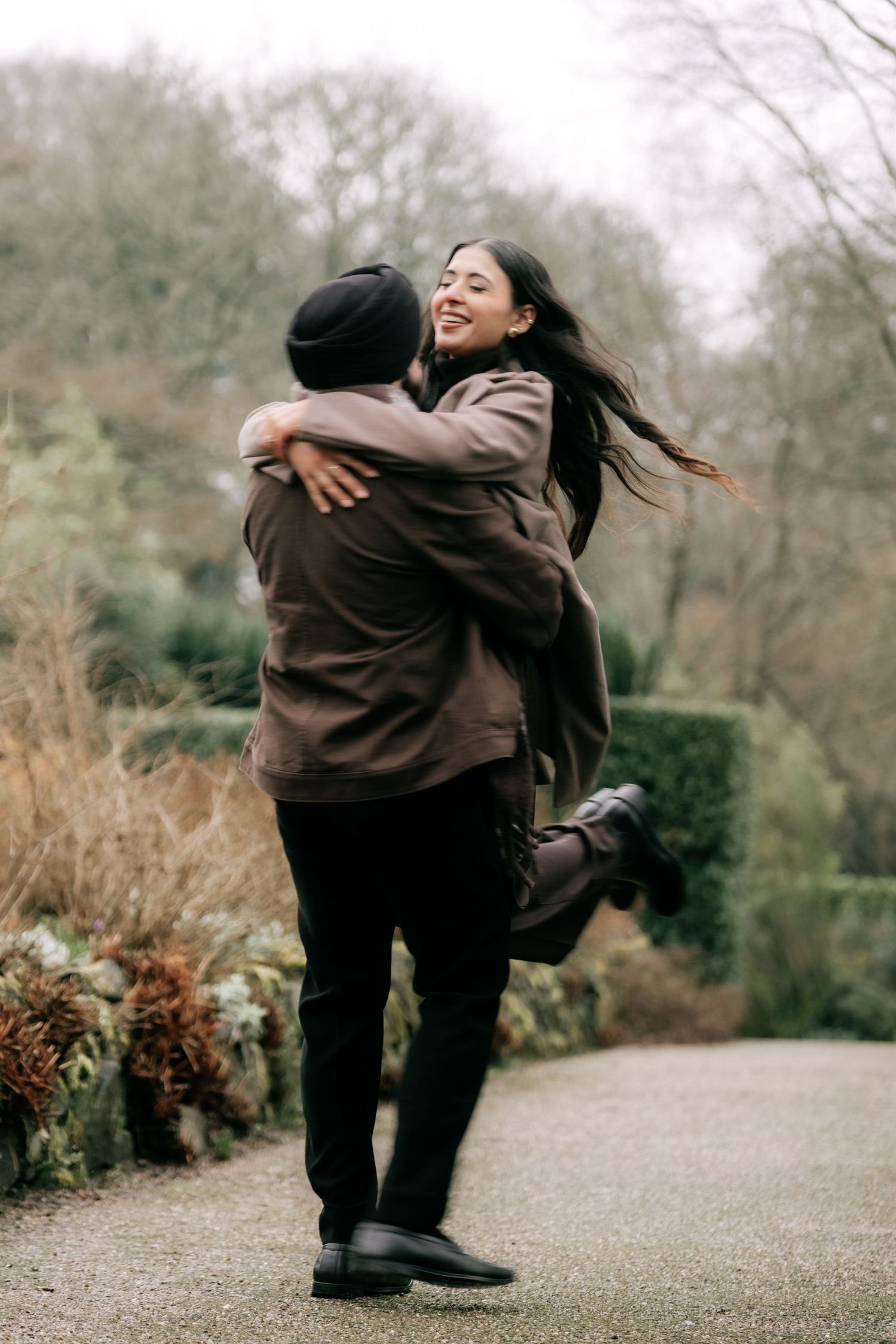A joyful embrace captured in a garden setting with winter foliage.