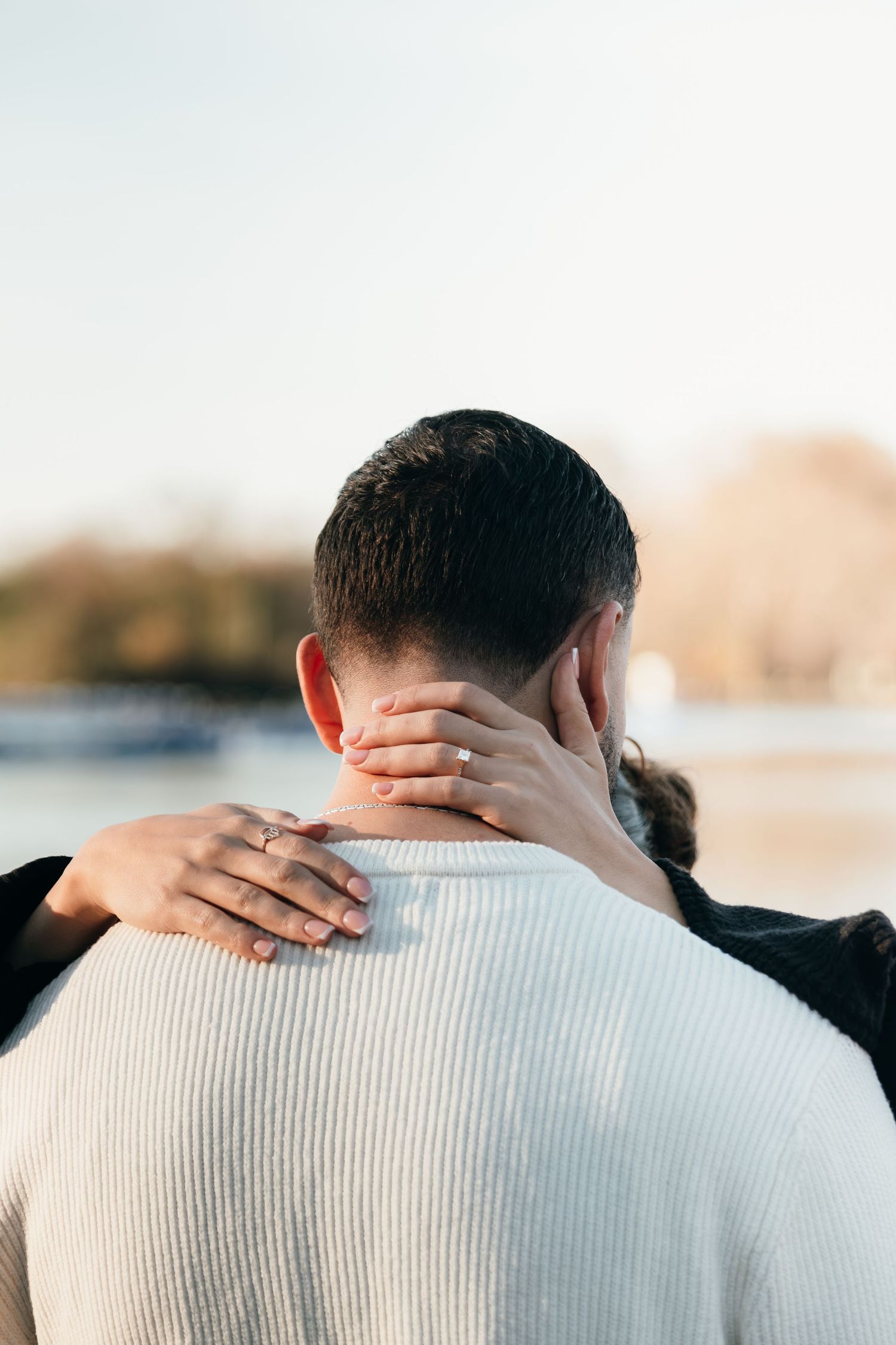 Close-up view of hands embracing on a white sweater during an intimate outdoor moment.