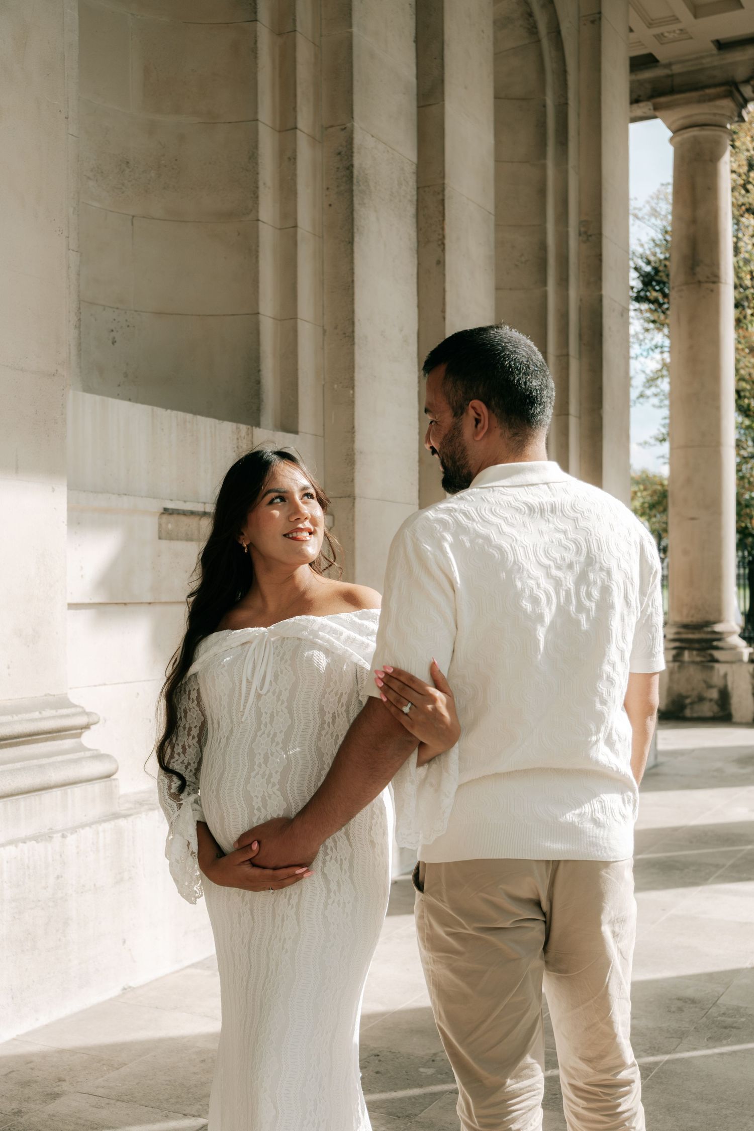 Romantic couple in white embracing among classical stone pillars.