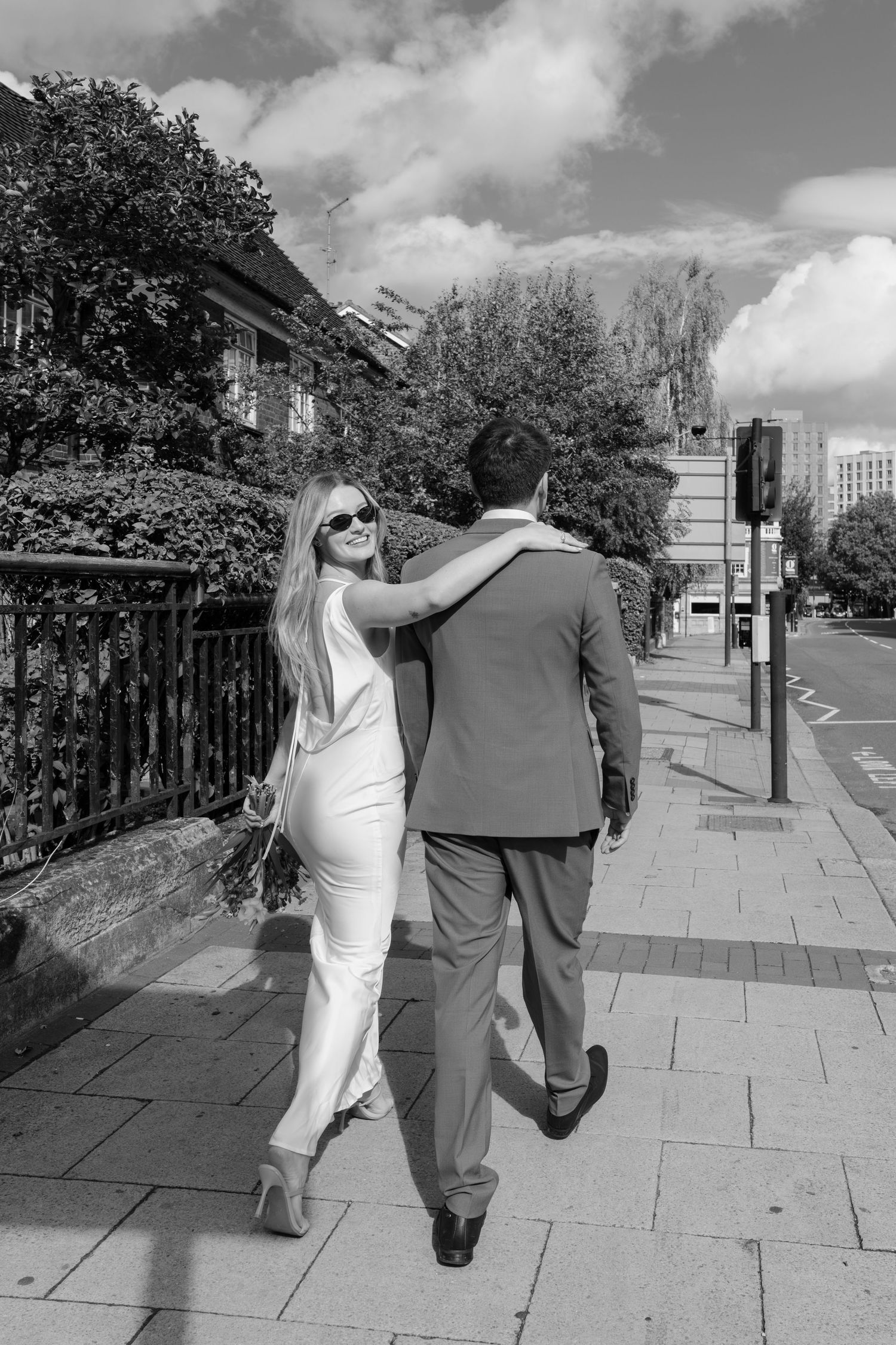 Black and white photos of newlyweds walking together on a sunny sidewalk.