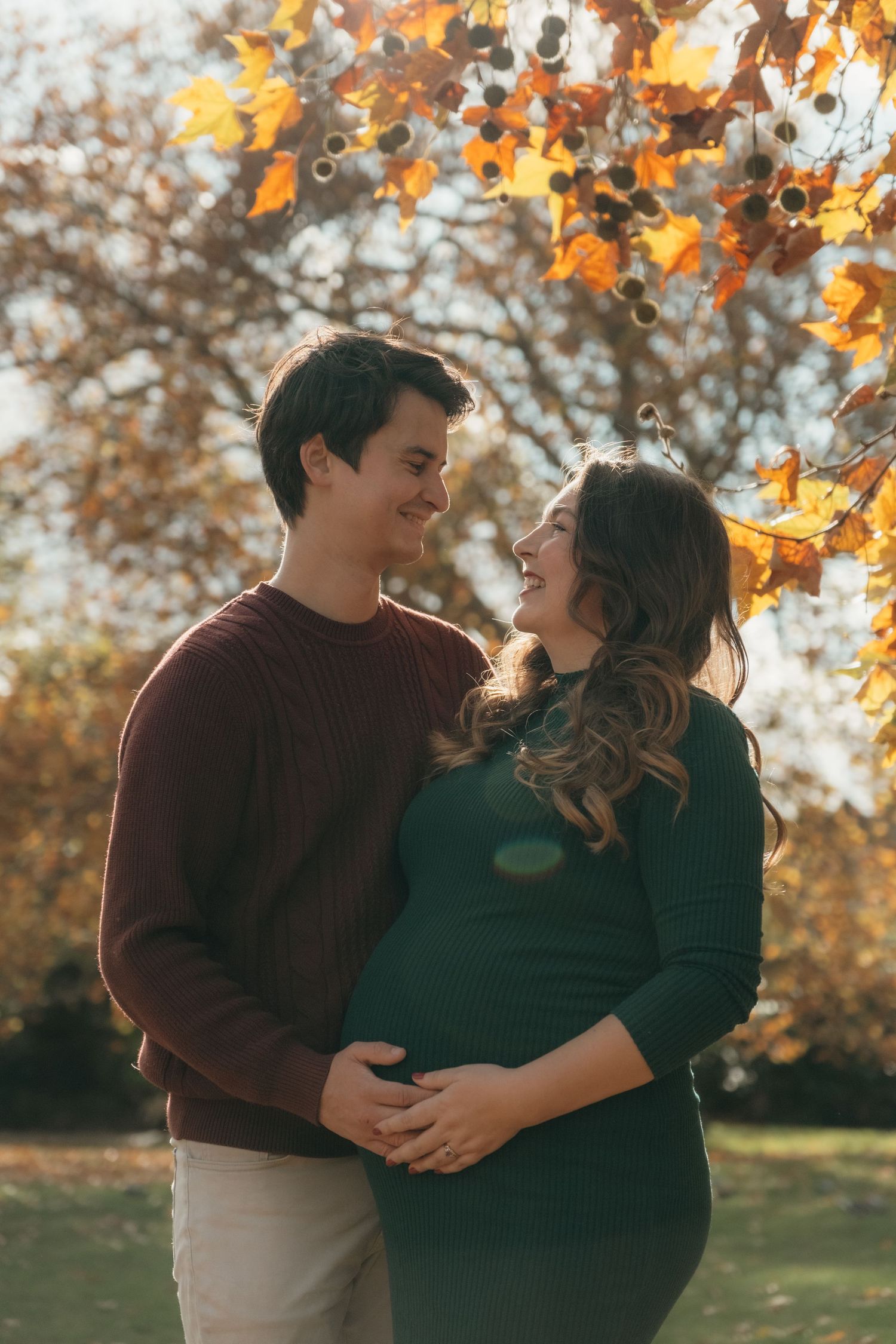 Couple embracing during fall maternity session with golden leaves in background.