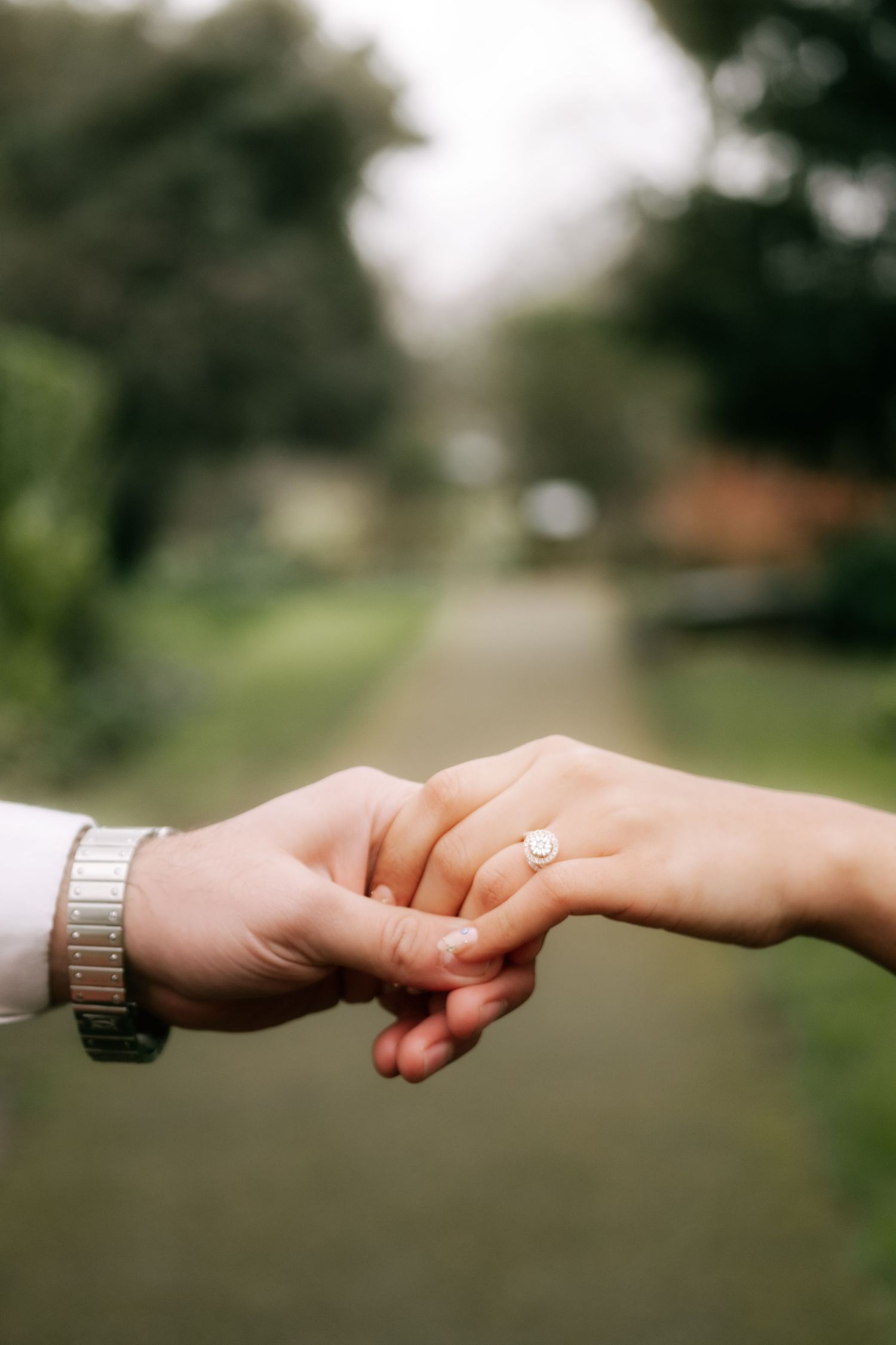 Close-up of hands holding with an engagement ring in a garden setting.