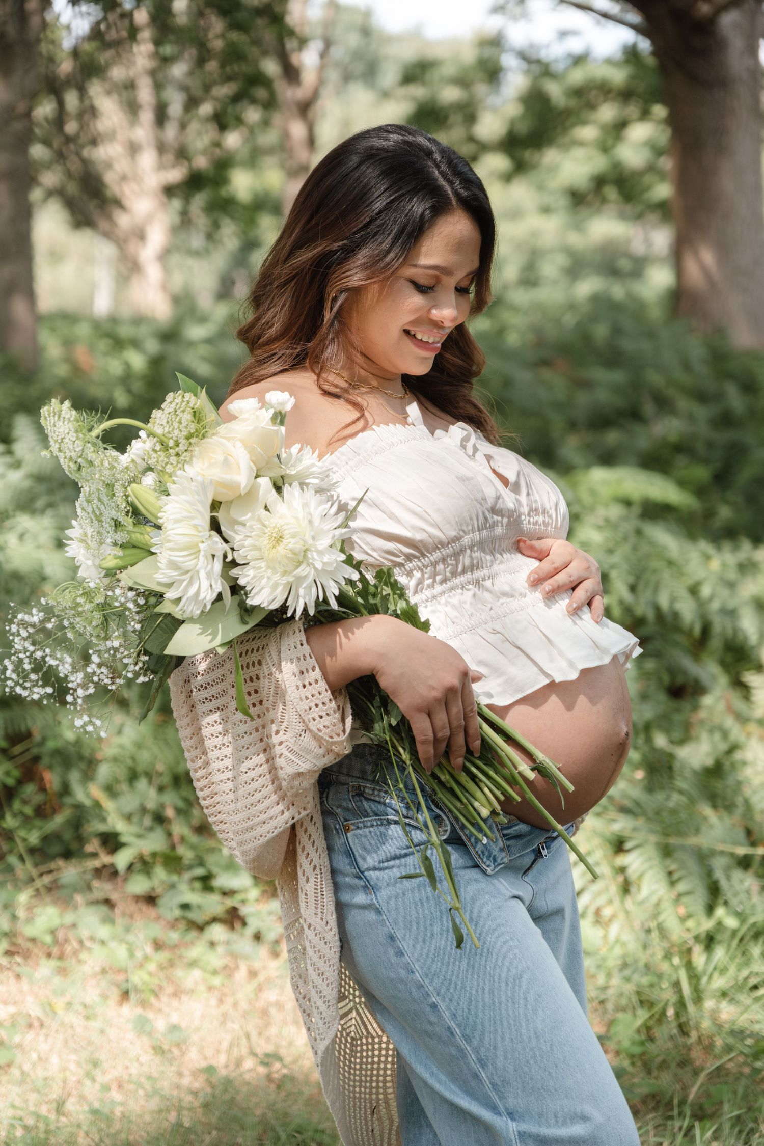 Natural maternity portraits with white flowers and casual attire in outdoor setting.