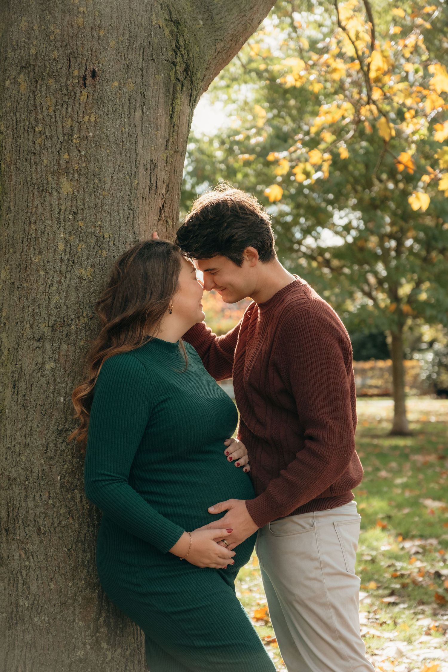 Intimate maternity photos of couple by large tree trunk during golden hour.
