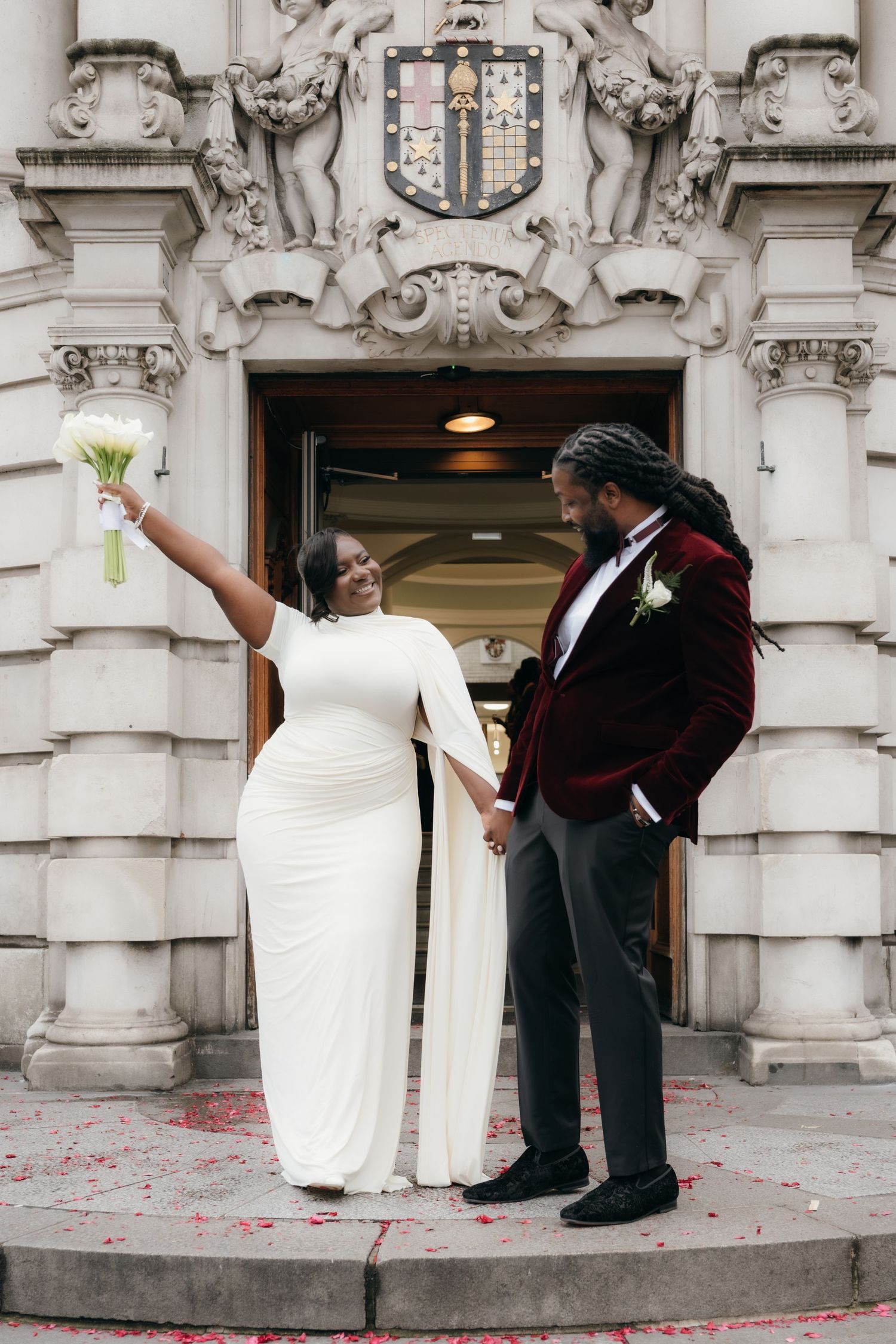 A couple celebrates their wedding exit on ornate stone steps while guests throw confetti.