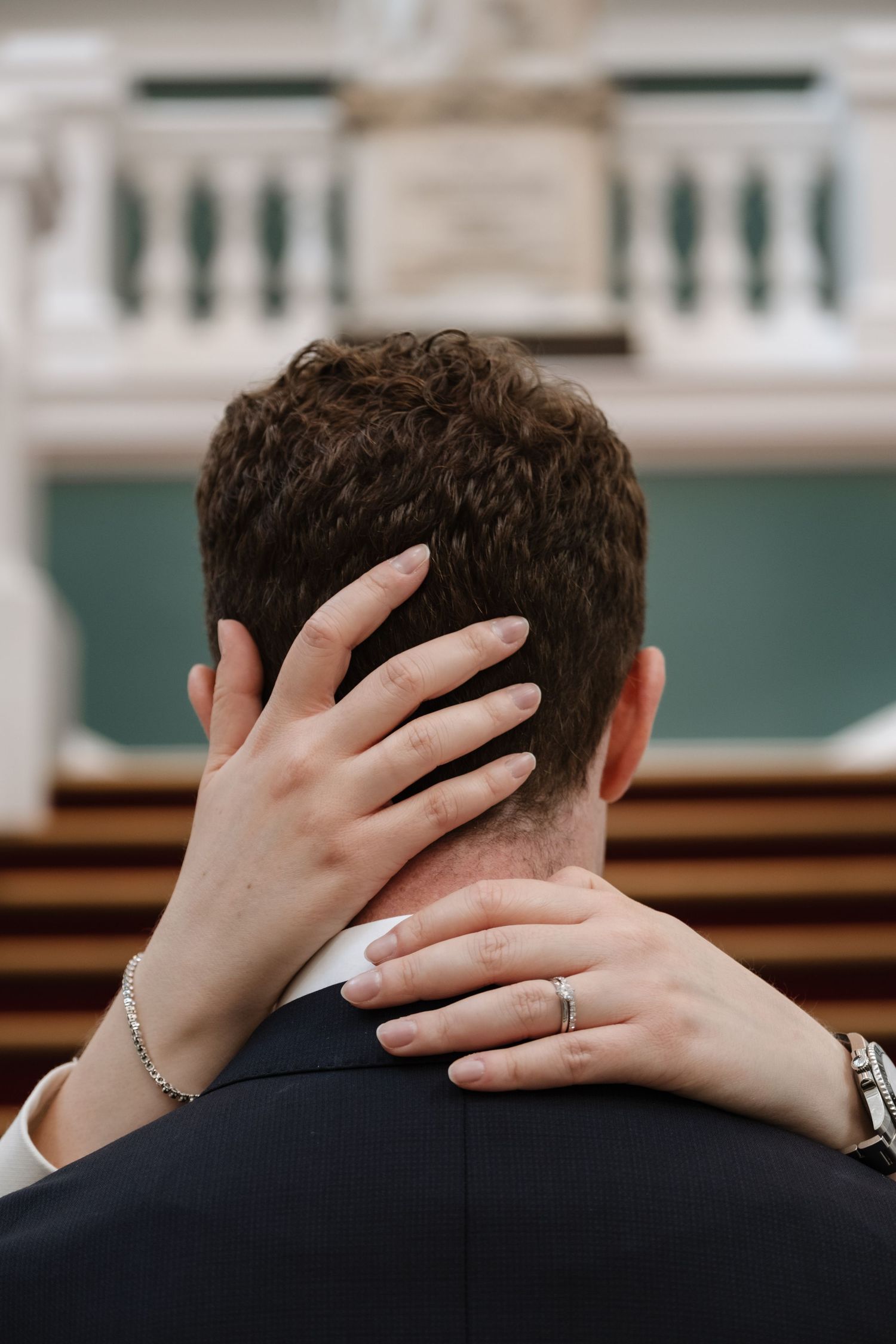 Bride's hand with wedding ring resting on groom's neck during wedding ceremony.