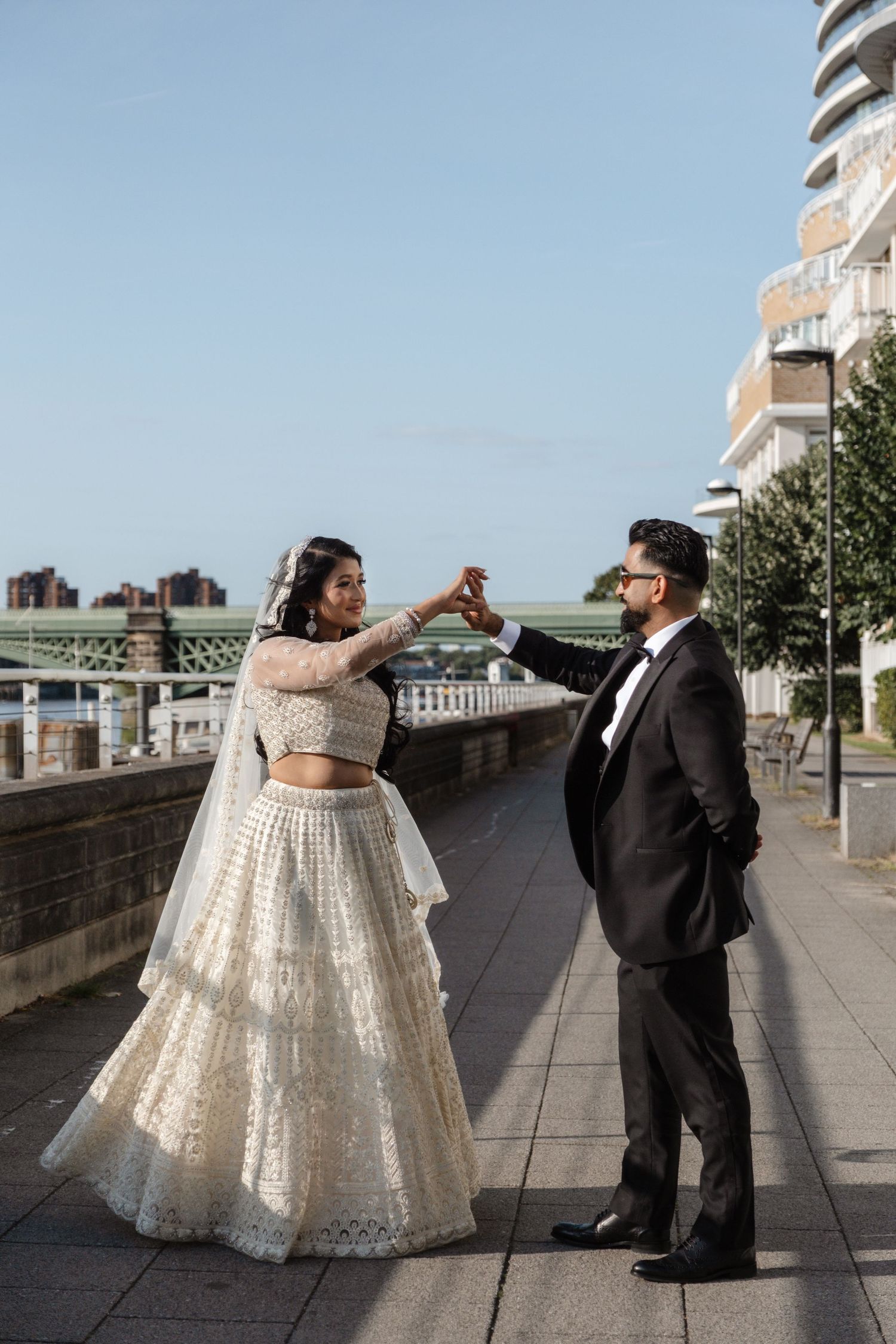 A couple in wedding attire shares a playful moment on an urban waterfront promenade.