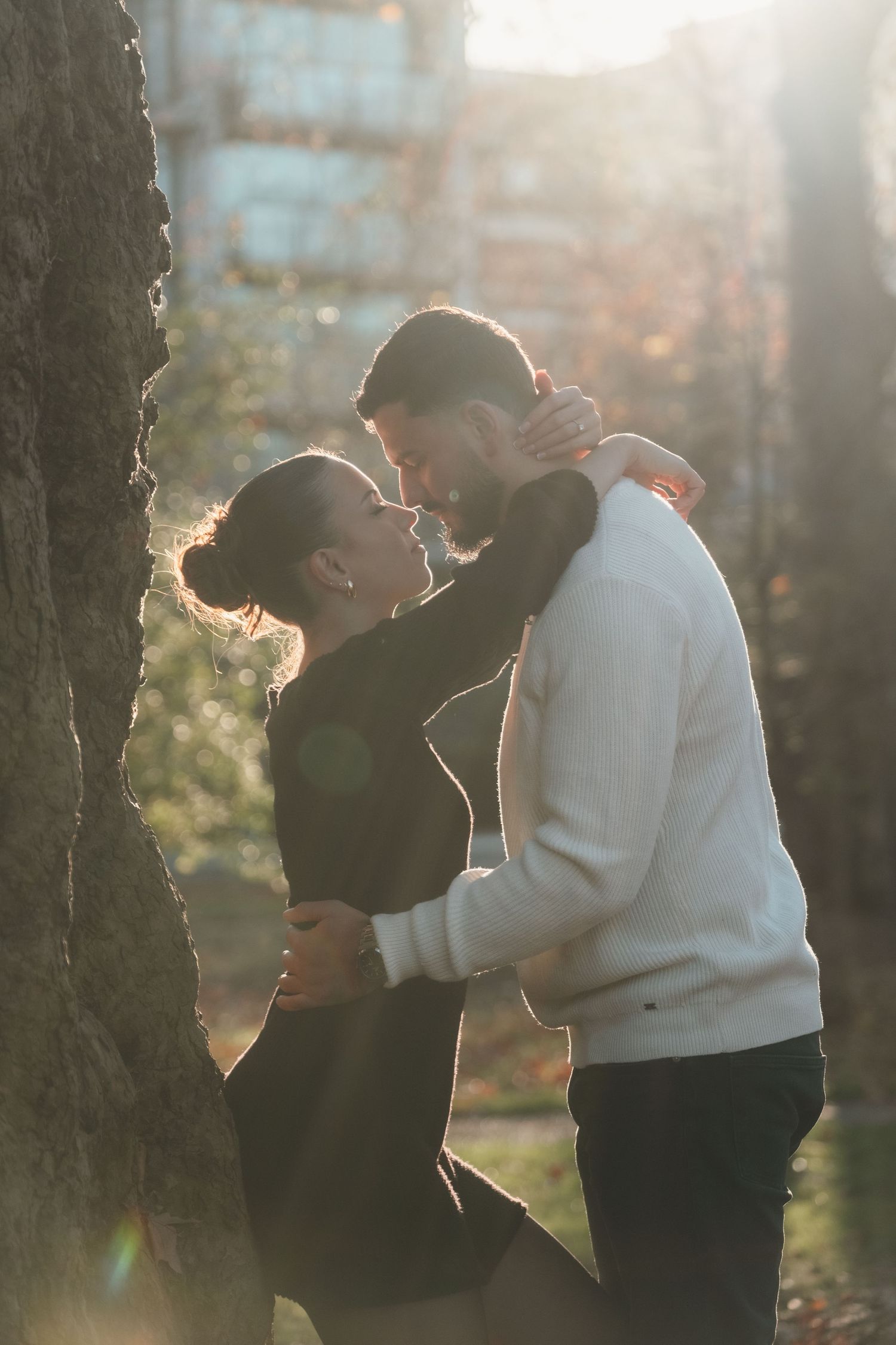 A couple embraces in golden sunlight against a tree trunk during autumn.