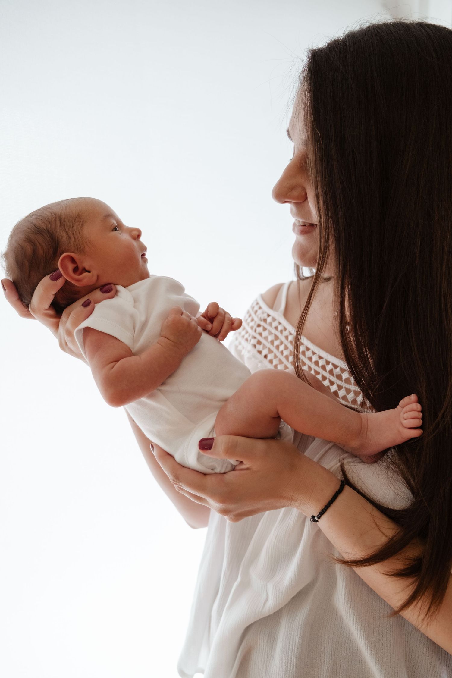 Tender moments between parent and newborn in white against bright background.