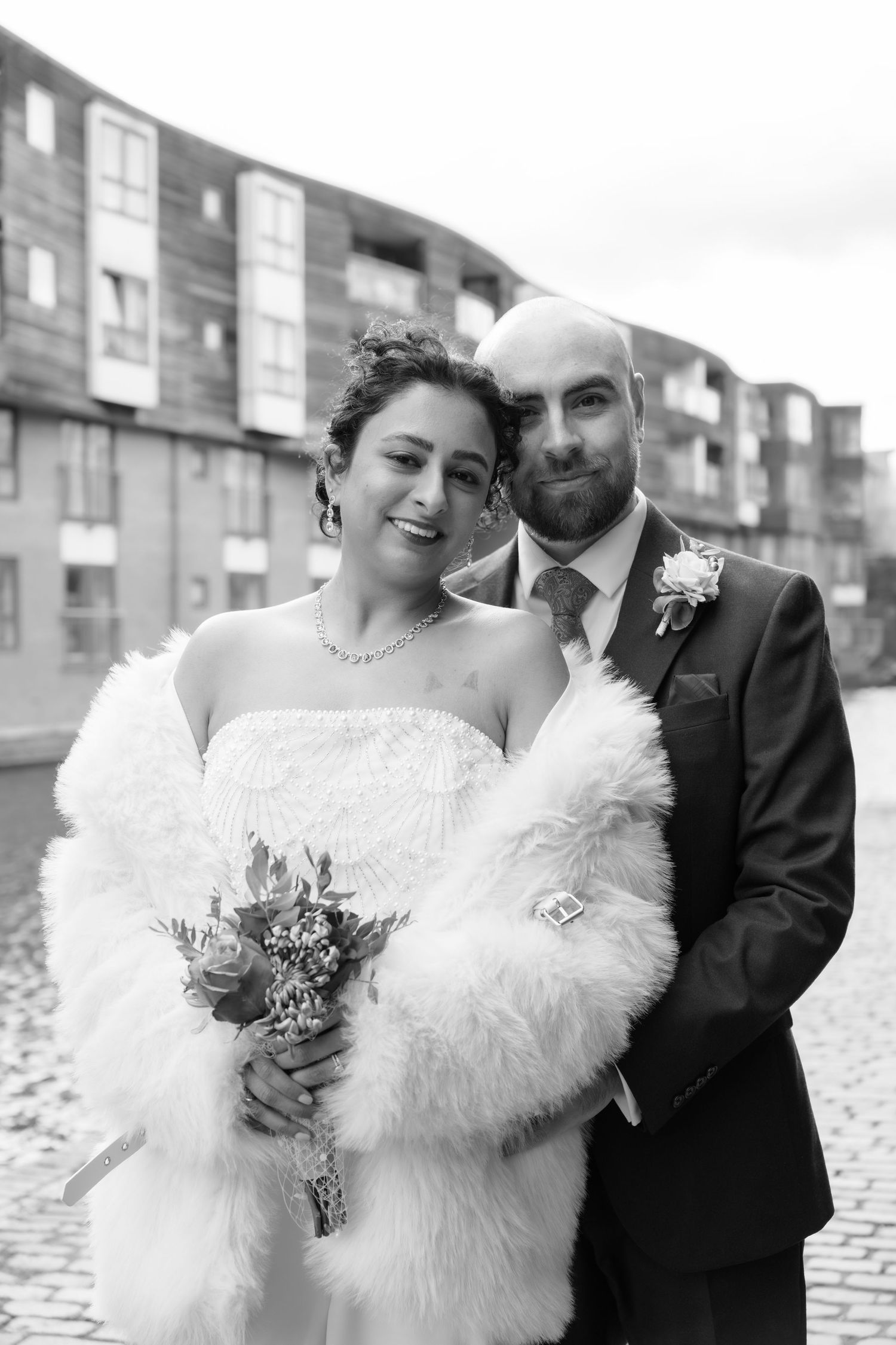 A black and white portrait of newlyweds posing together on cobblestone streets.